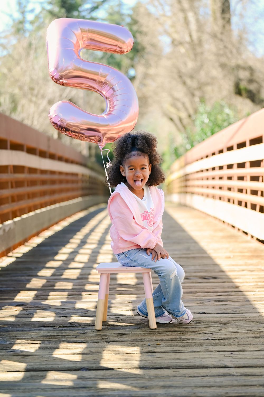 Child playing with pink balloon on wooden boardwalk during sunny day.