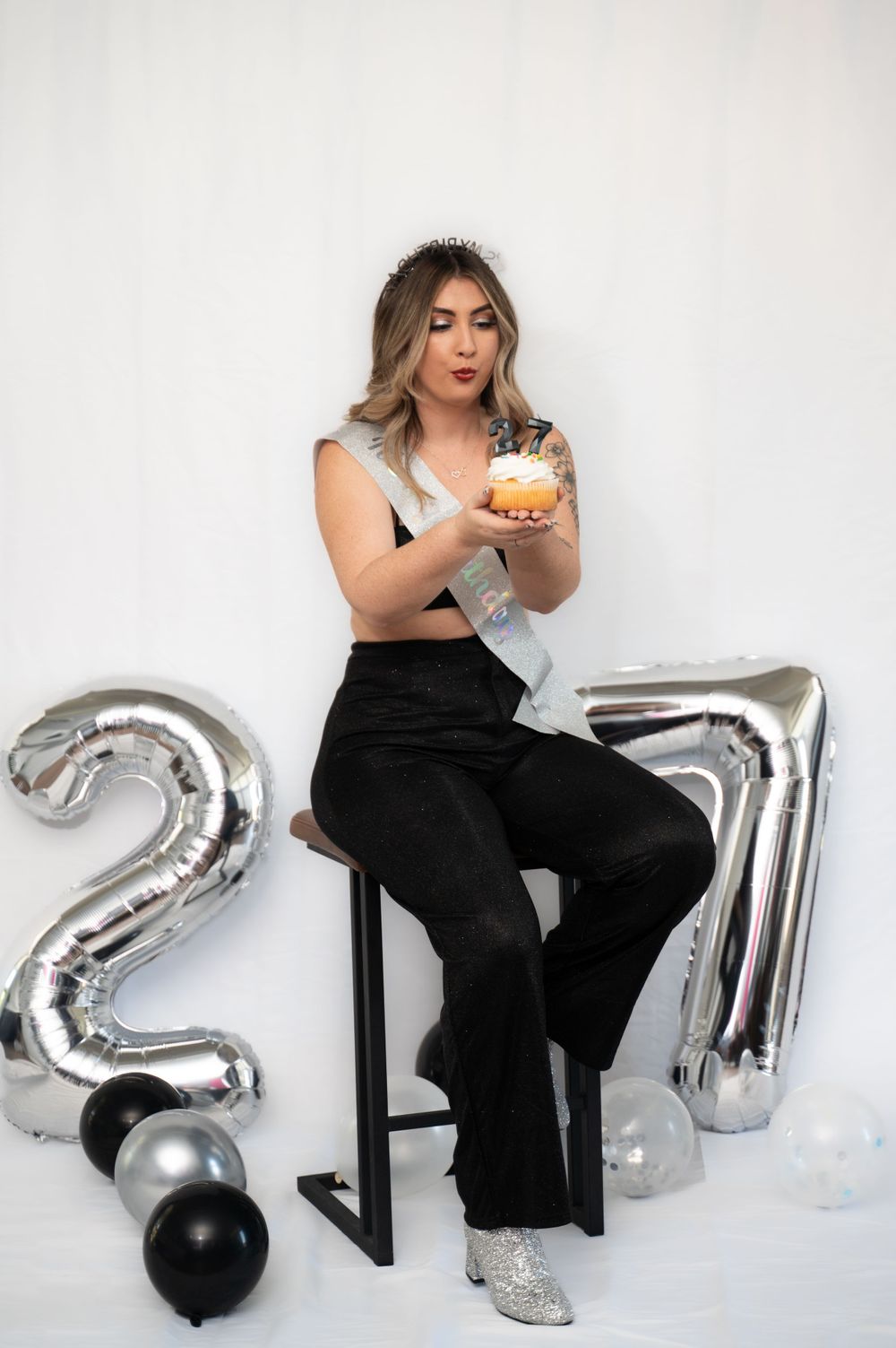 A celebratory photo shoot with silver number balloons and black and silver decorations.