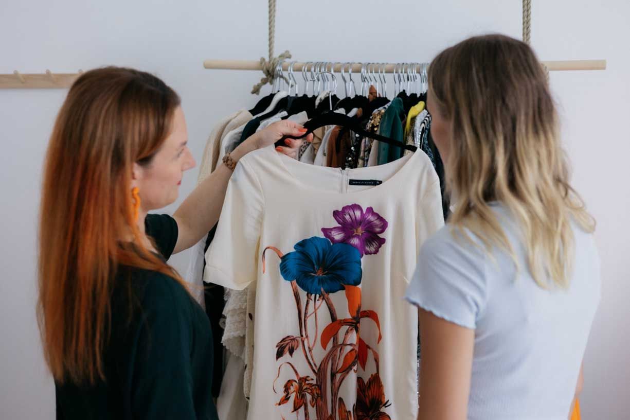 Two people looking through clothing on a rack featuring a t-shirt with a colorful floral design.