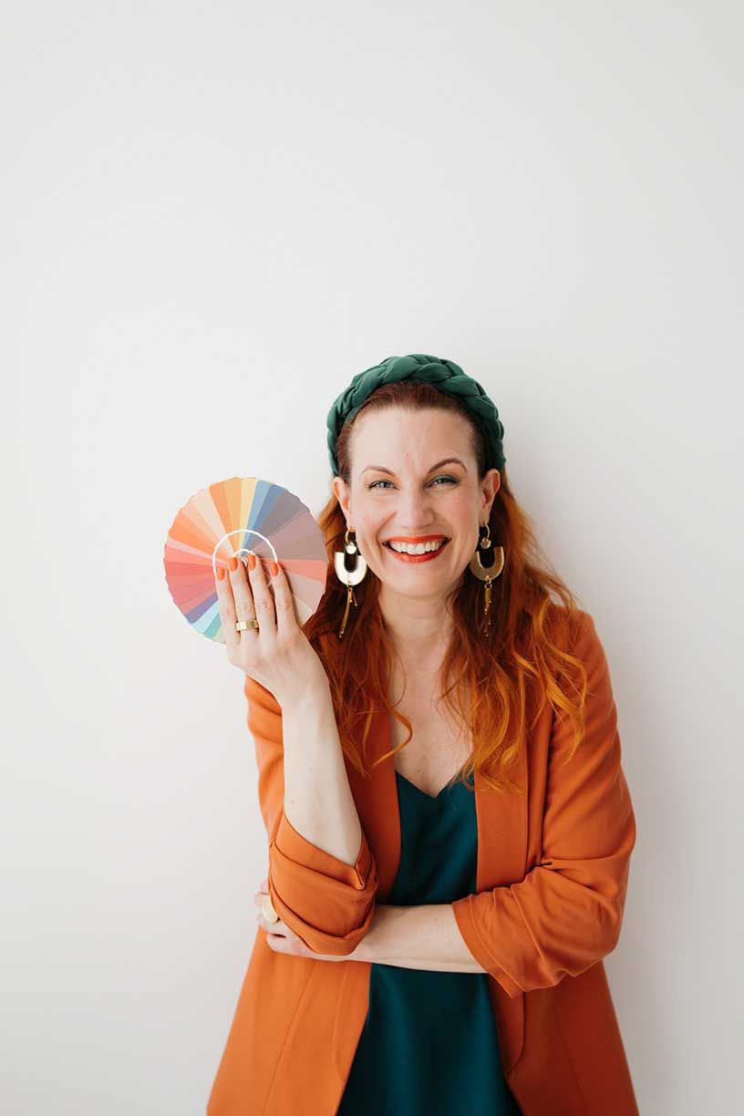 Professional wearing an orange blazer holds color swatches against a white background in a creative photo series.
