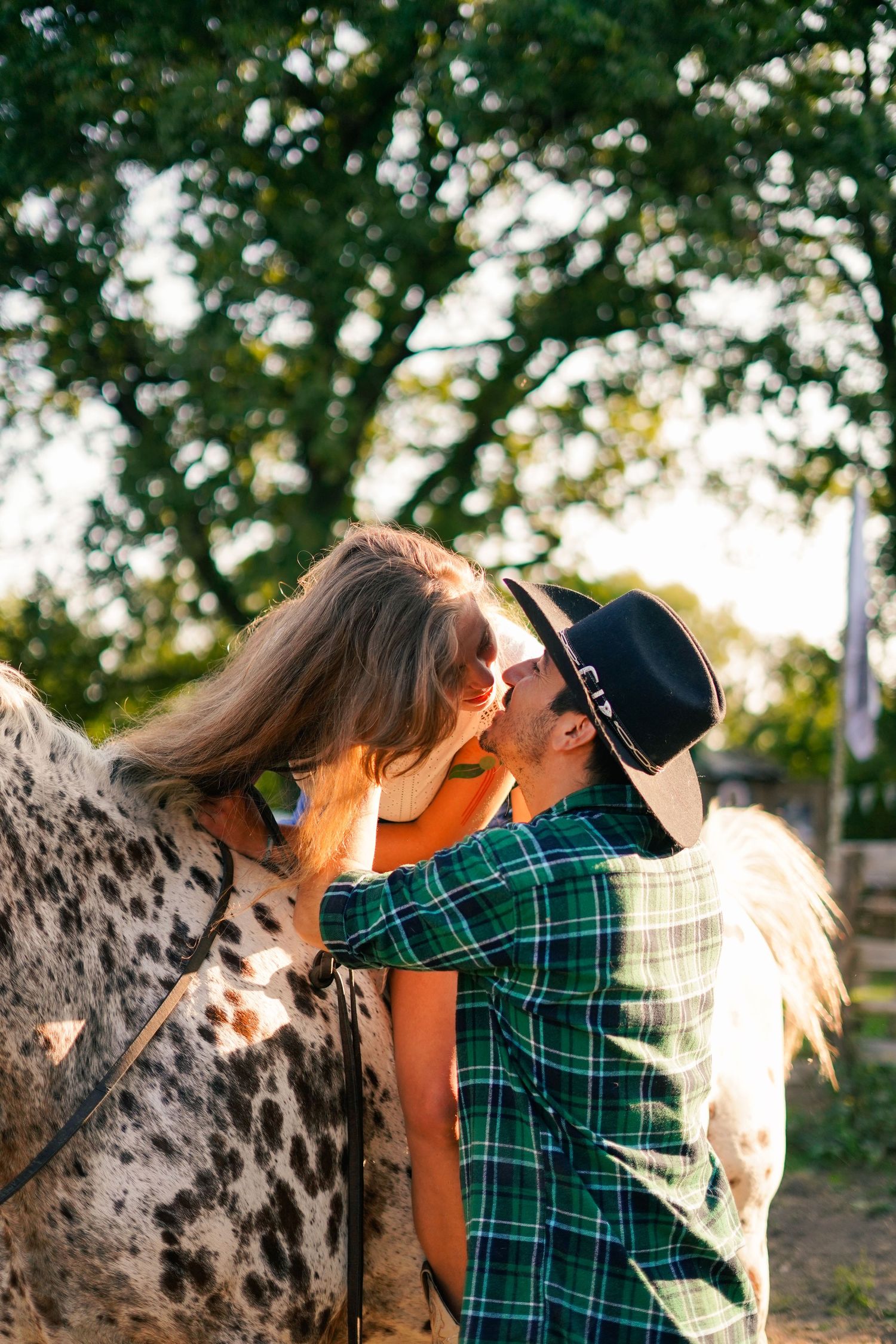 A couple shares an intimate moment near a spotted horse in warm sunlight.