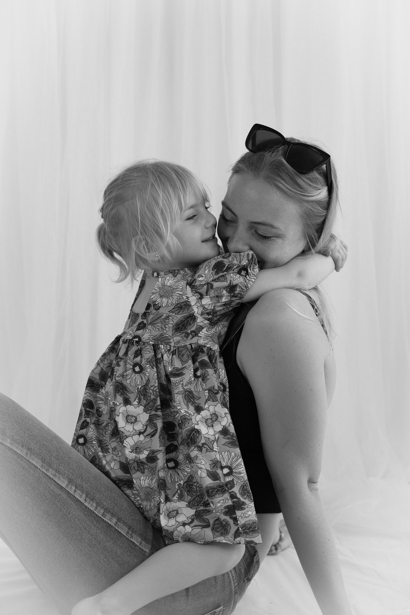 Black and white portrait showing an intimate moment between two people against a white backdrop.
