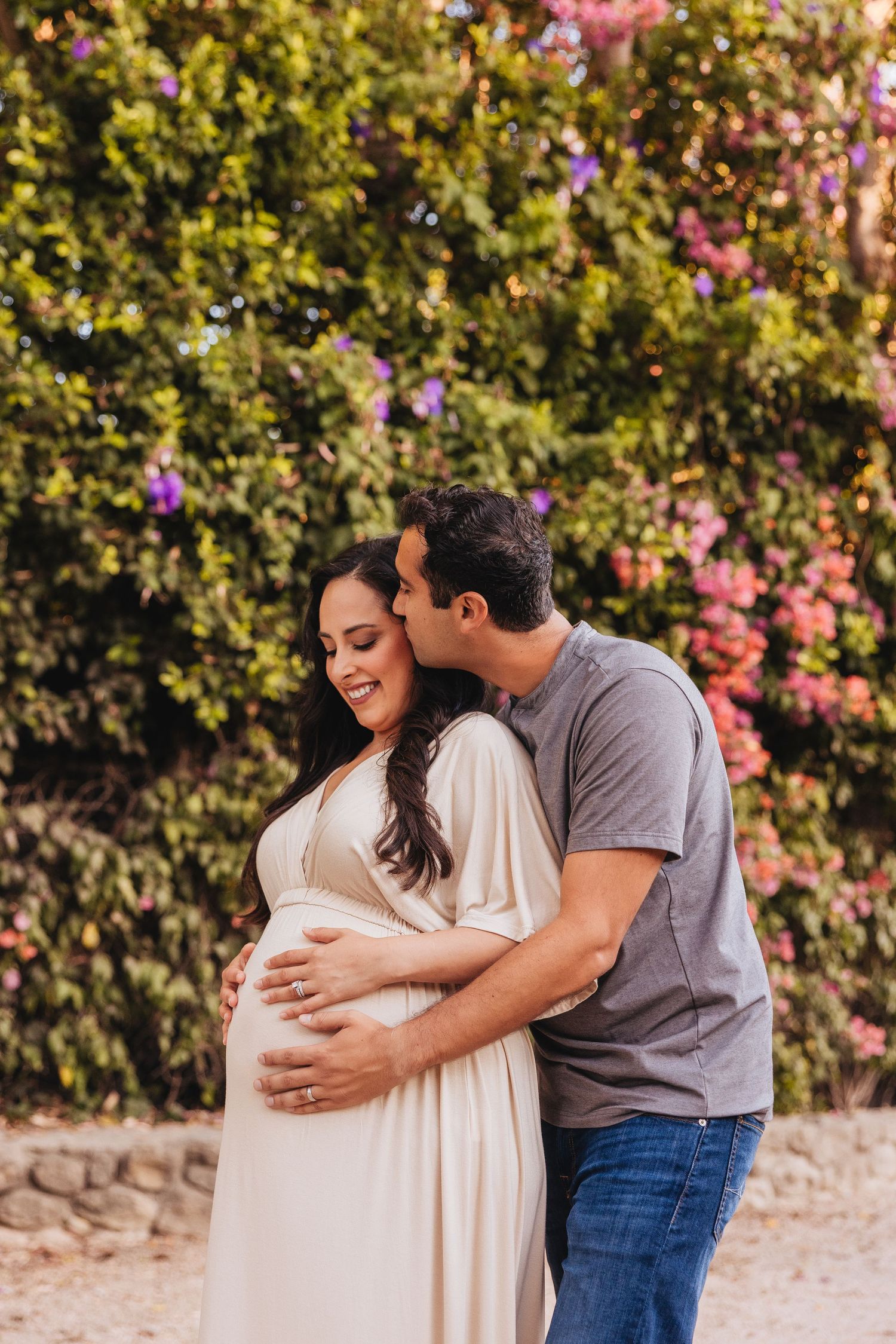 Maternity photo session in front of flowering bushes and greenery.