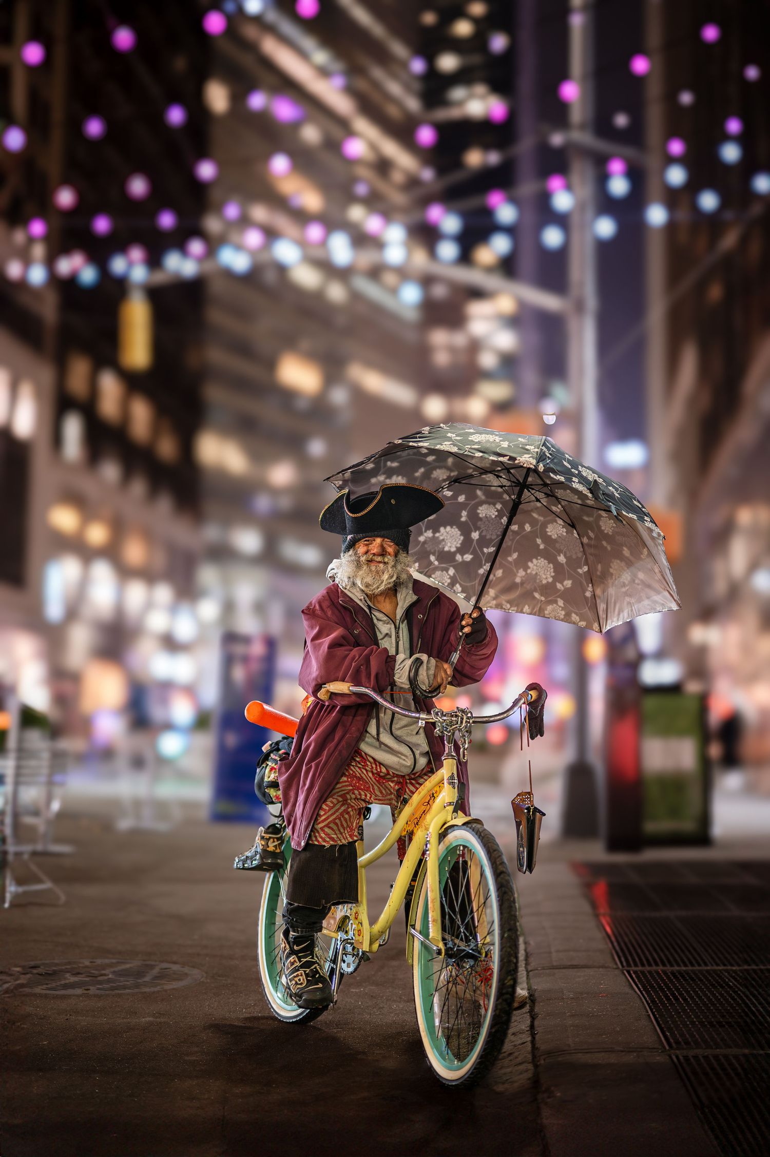 Cyclist with umbrella riding yellow bike under colorful city lights at night.