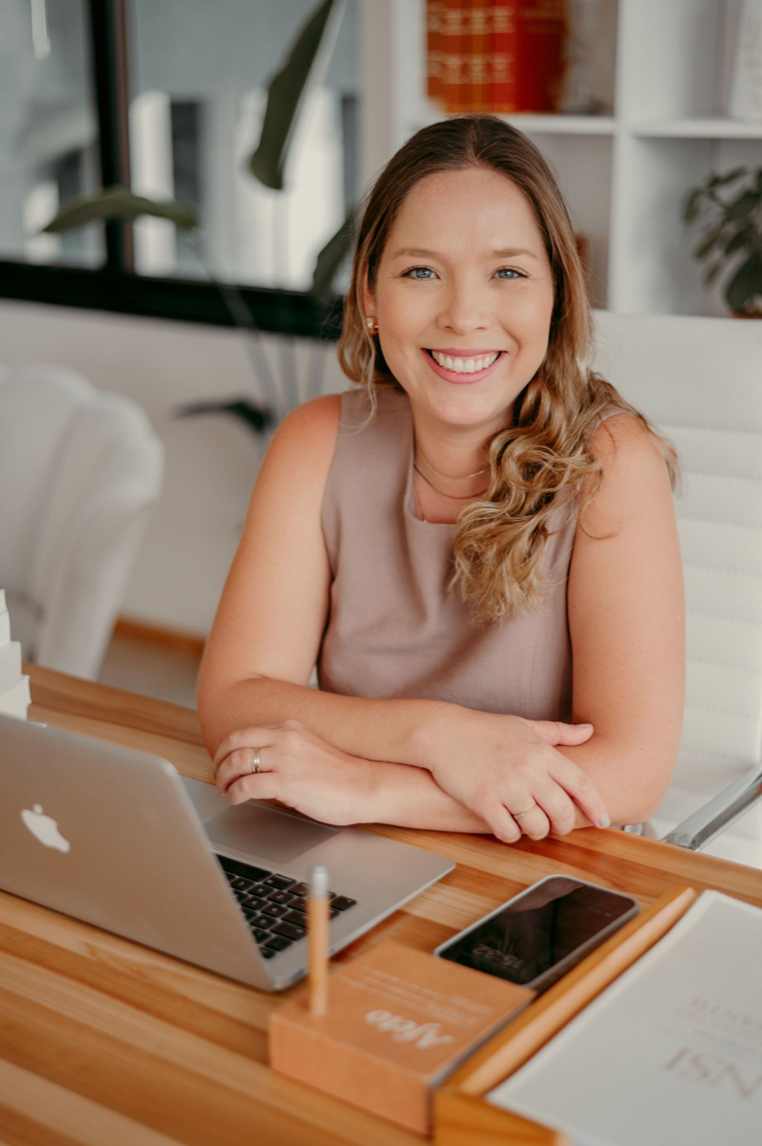 Woman smiles while working at wooden desk with laptop and modern office decor.