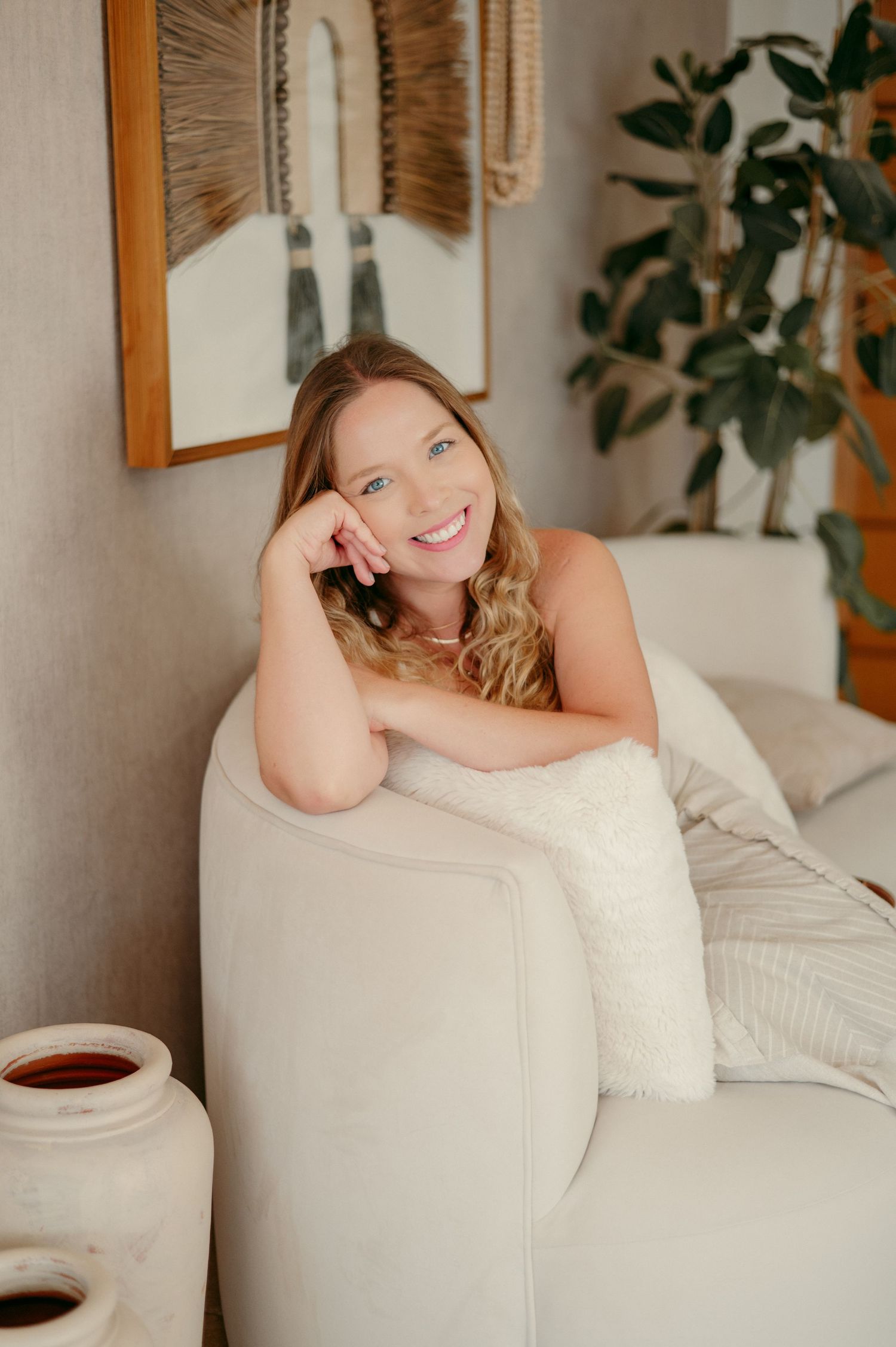 Lifestyle portrait of woman lounging on white chair in cozy home setting with plants.