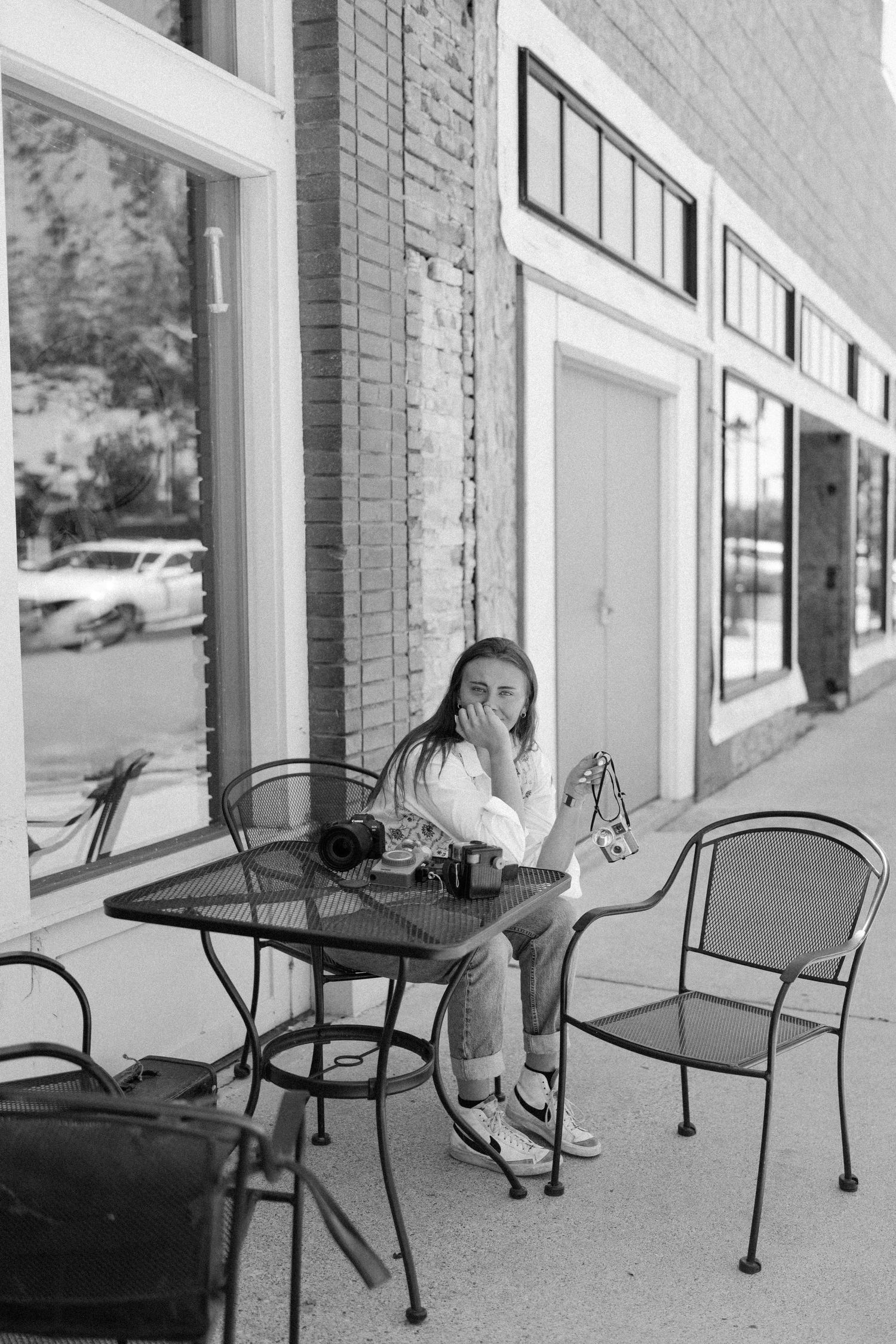Person sitting solo at outdoor cafe table with vintage camera in monochrome.