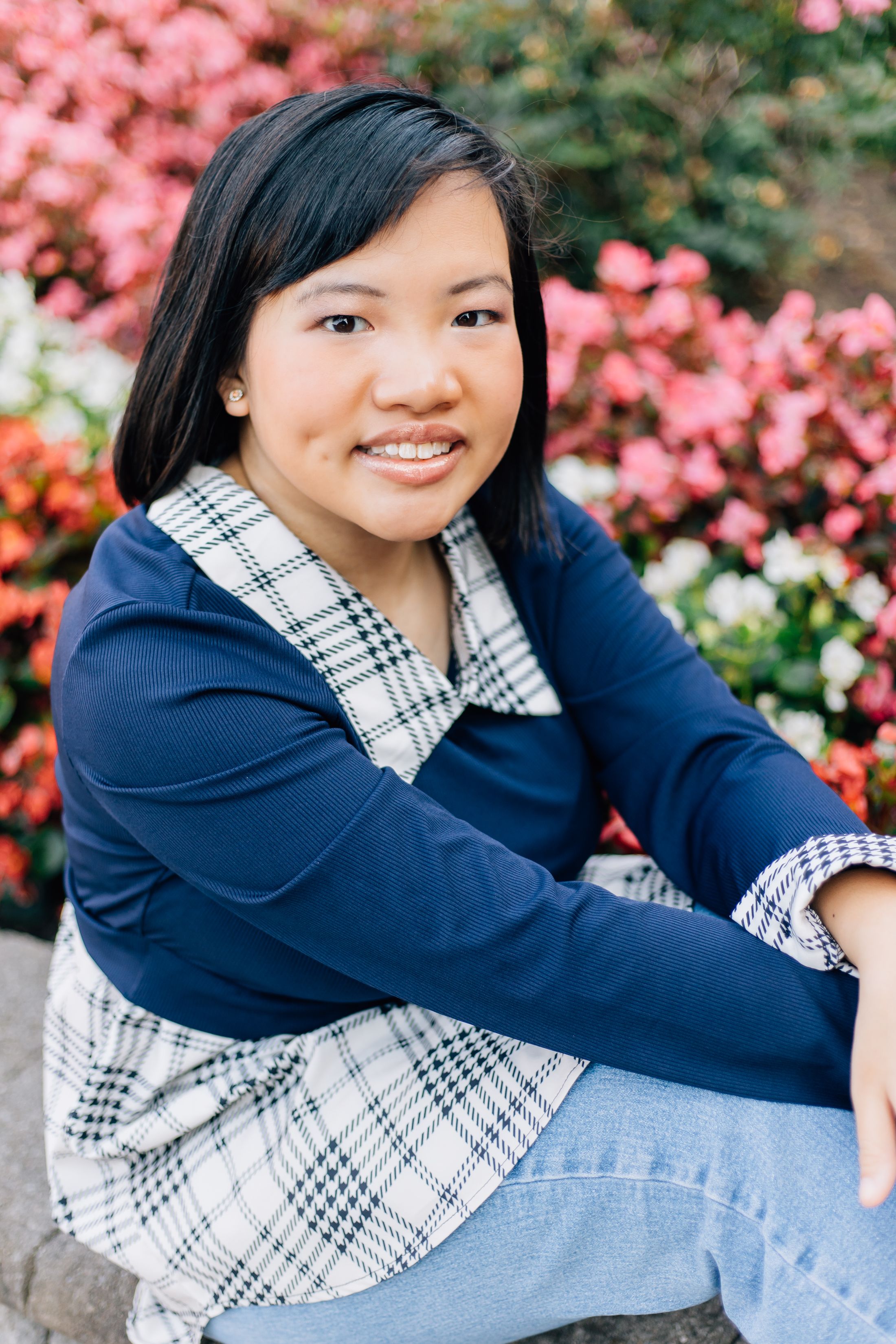 Spring portrait among pink azalea blooms wearing a navy cardigan and plaid dress.