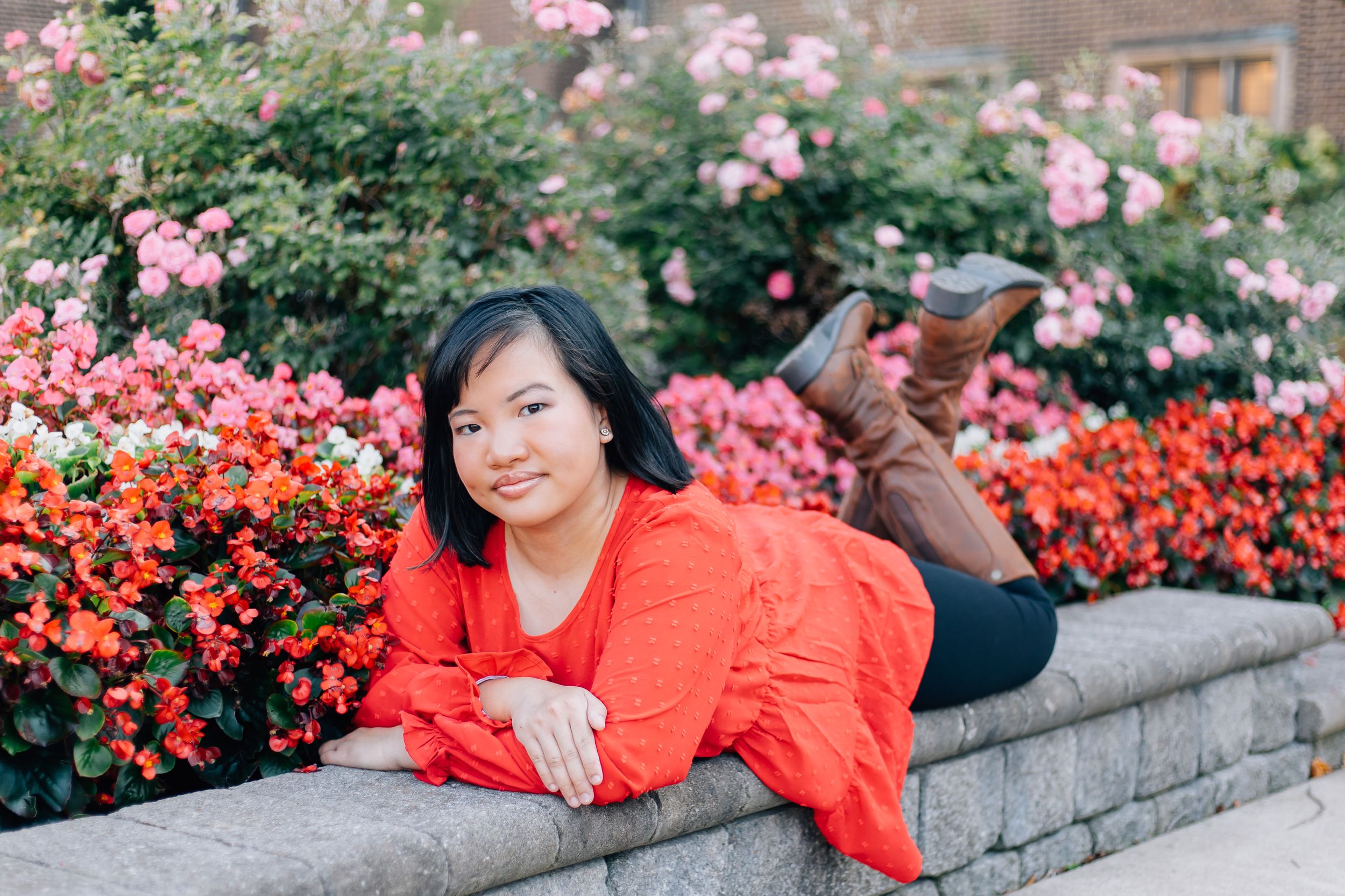 Casual portrait laying on stone wall surrounded by pink and coral flowering bushes.