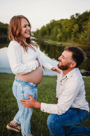 A couple shares a joyful moment together outdoors near a lake during a photo session in natural lighting.
