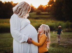 A parent and child share a tender moment outdoors during golden hour sunset in a grassy field.