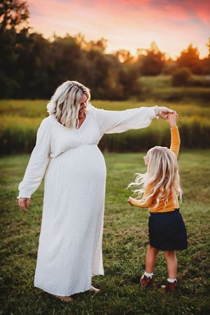Two people in white and blue outfits dance together joyfully in a grassy field at sunset.
