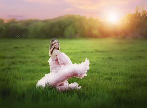 Ethereal sunset photoshoot in a lush green meadow with flowing pink dress creating a dreamy atmosphere.