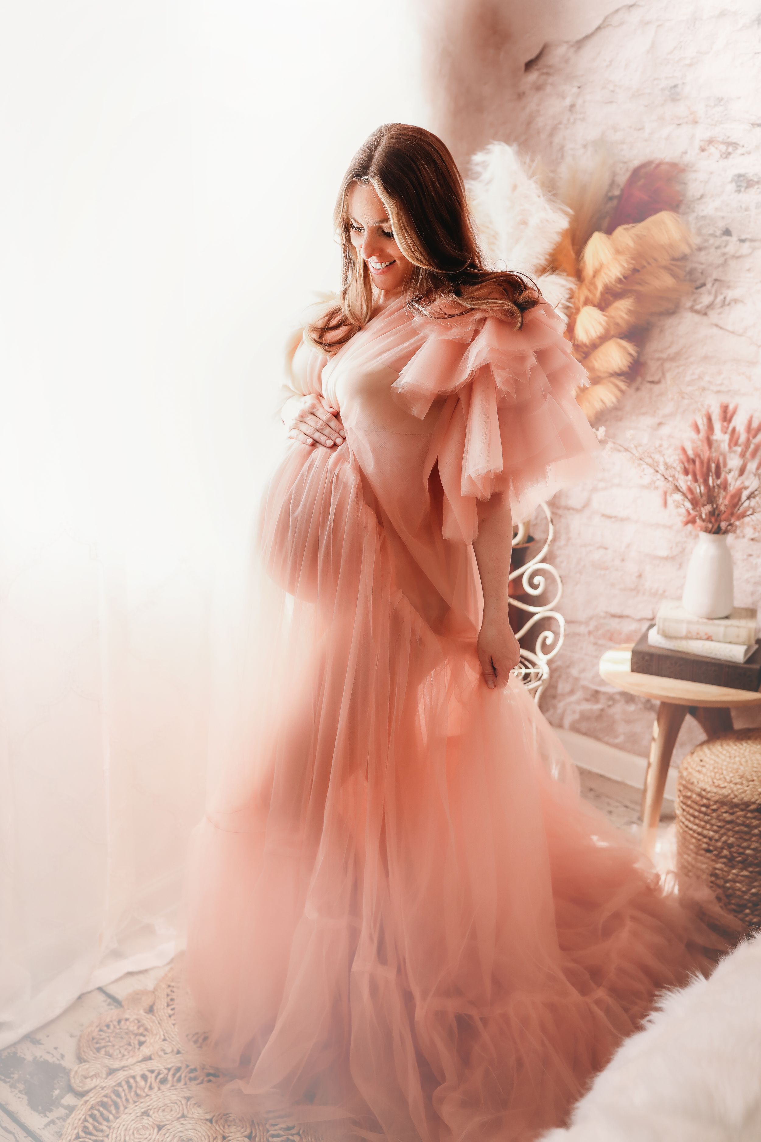 A dreamy peach-colored tulle dress flows elegantly in a romantic indoor setting with soft natural lighting.
