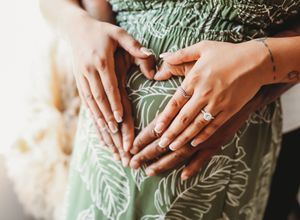Close-up details of hands holding delicate sage green fabric with intricate embroidered patterns.