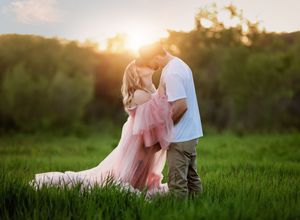 A couple embraces in a sunlit meadow during golden hour with tall grass surrounding them.