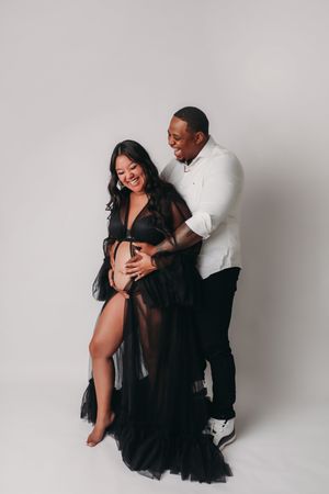 Romantic couple in black outfits sharing intimate moments in minimalist white studio setting across multiple poses.