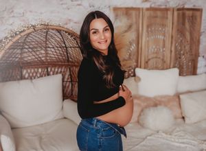 A person in a black crop top and jeans poses against a cozy neutral backdrop with white pillows and woven decor.