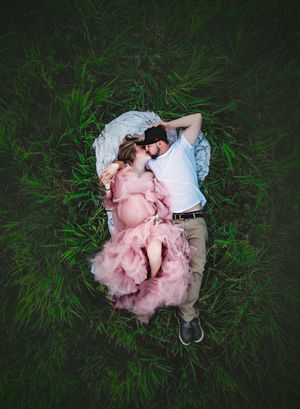Aerial view of a couple lying together in tall green grass wearing pink tulle dress and casual attire.