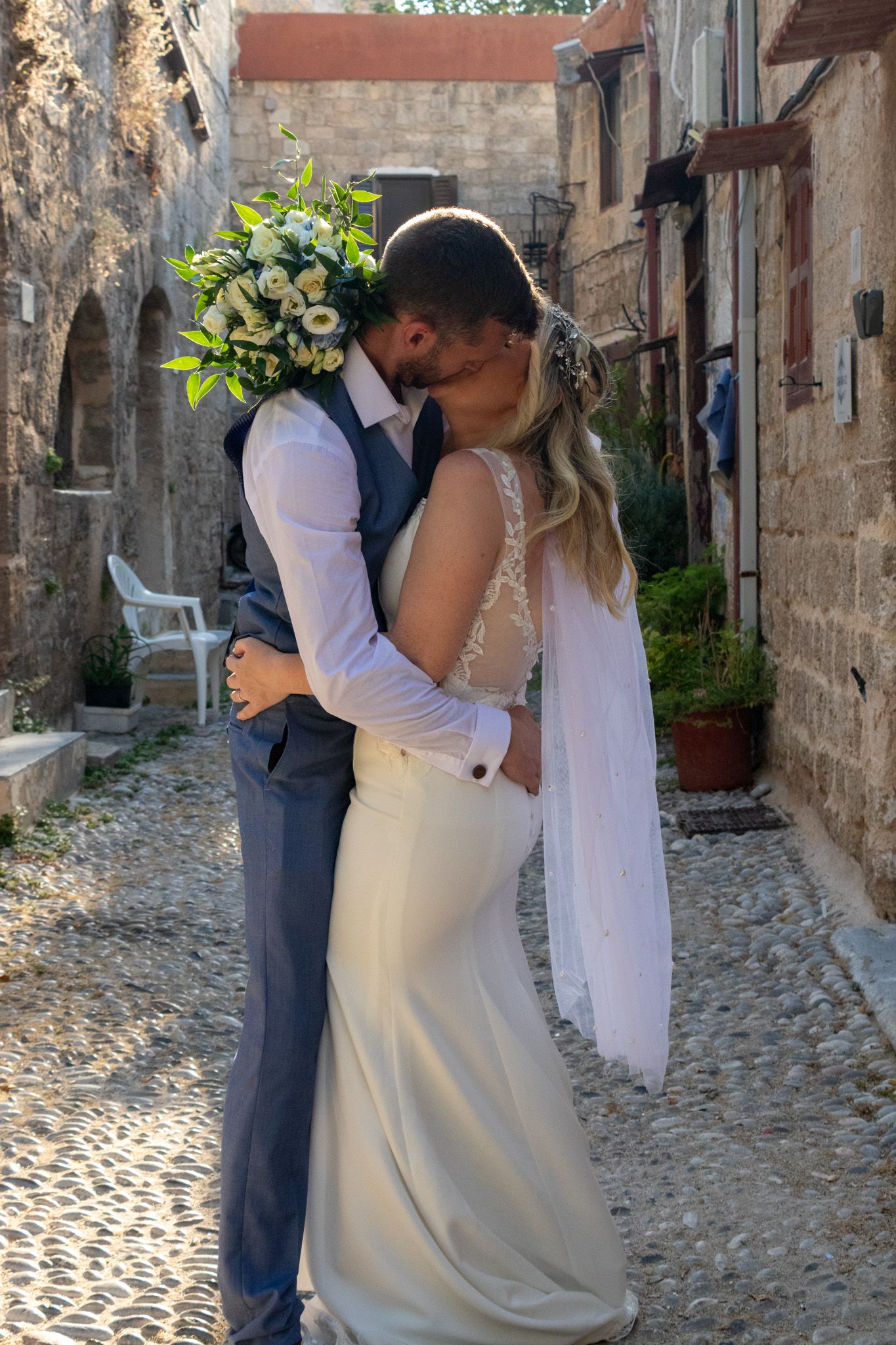 A romantic moment between newlyweds in a charming cobblestone alley with bouquet.