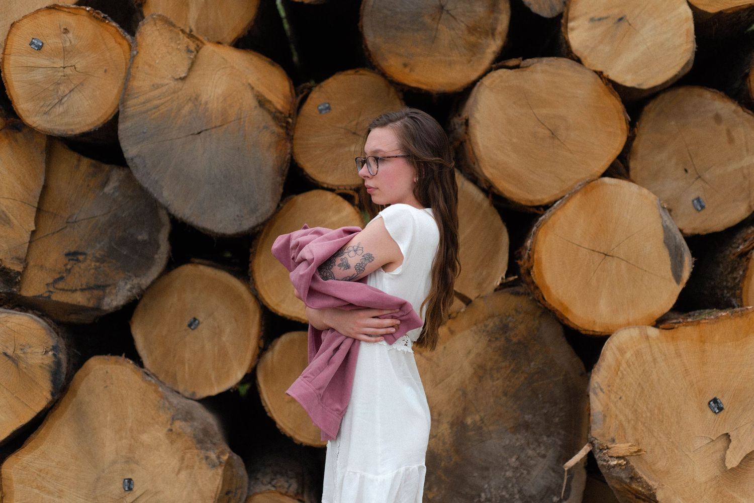 Figure in white dress holds baby against rustic background of stacked logs.