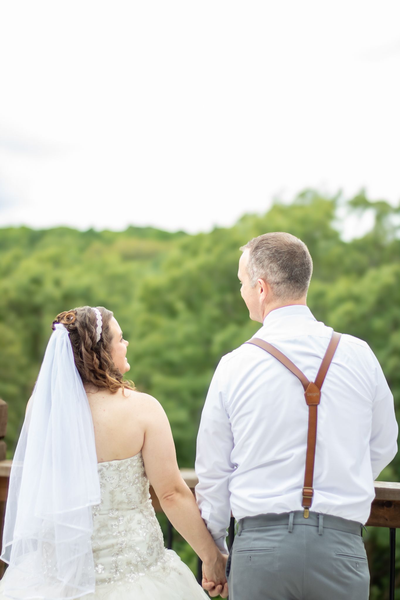 Bride and groom holding hands smiling at each other at their wedding in front of trees.