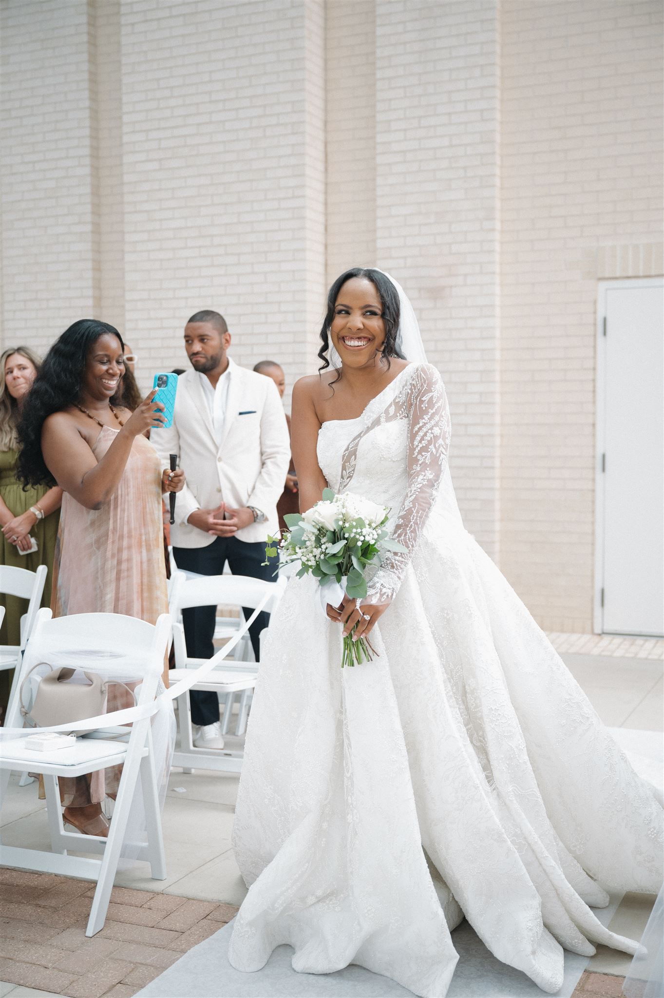 A joyful moment at an elegant outdoor wedding ceremony with a stunning white lace gown and cascading bouquet.