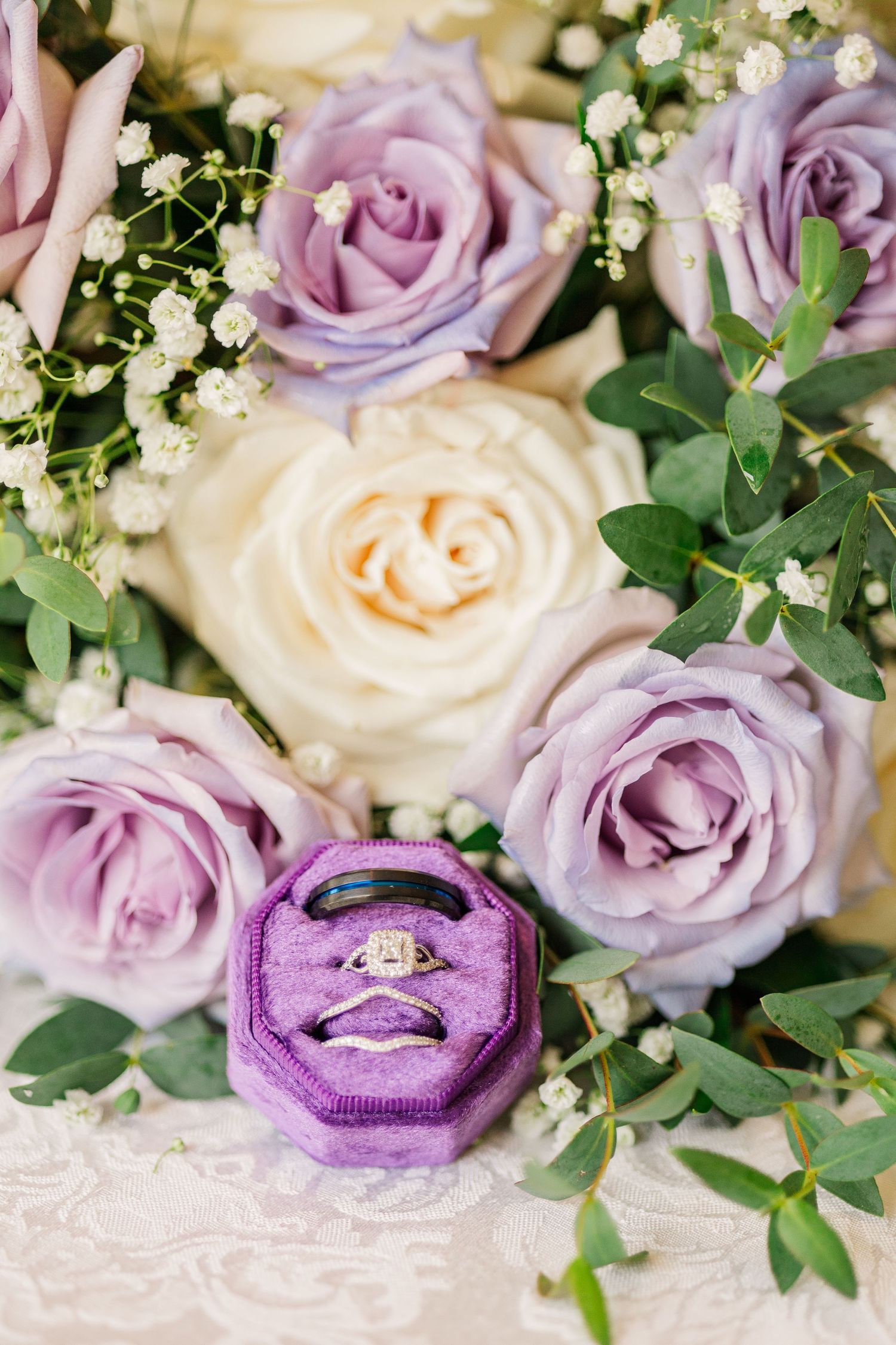 Purple and cream roses surround an engagement ring in a velvet purple box.