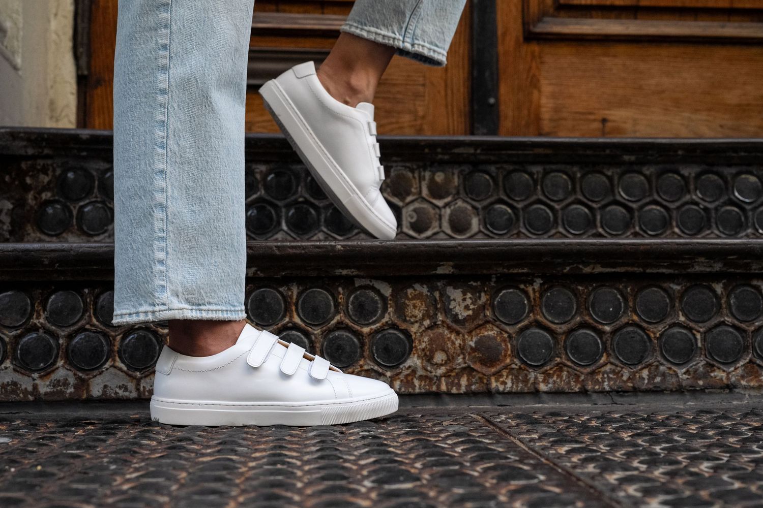 Close-up of white sneakers and light denim jeans on decorative metal grating.
