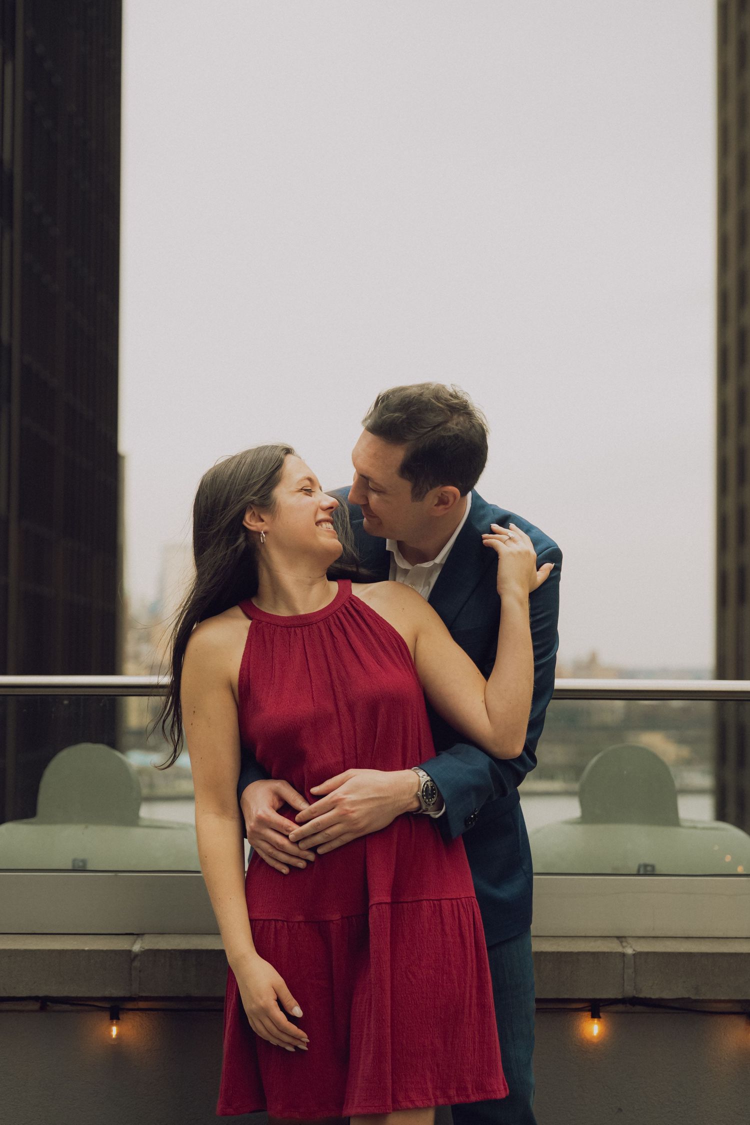 Couple sharing intimate moment on balcony with one person wearing burgundy dress.