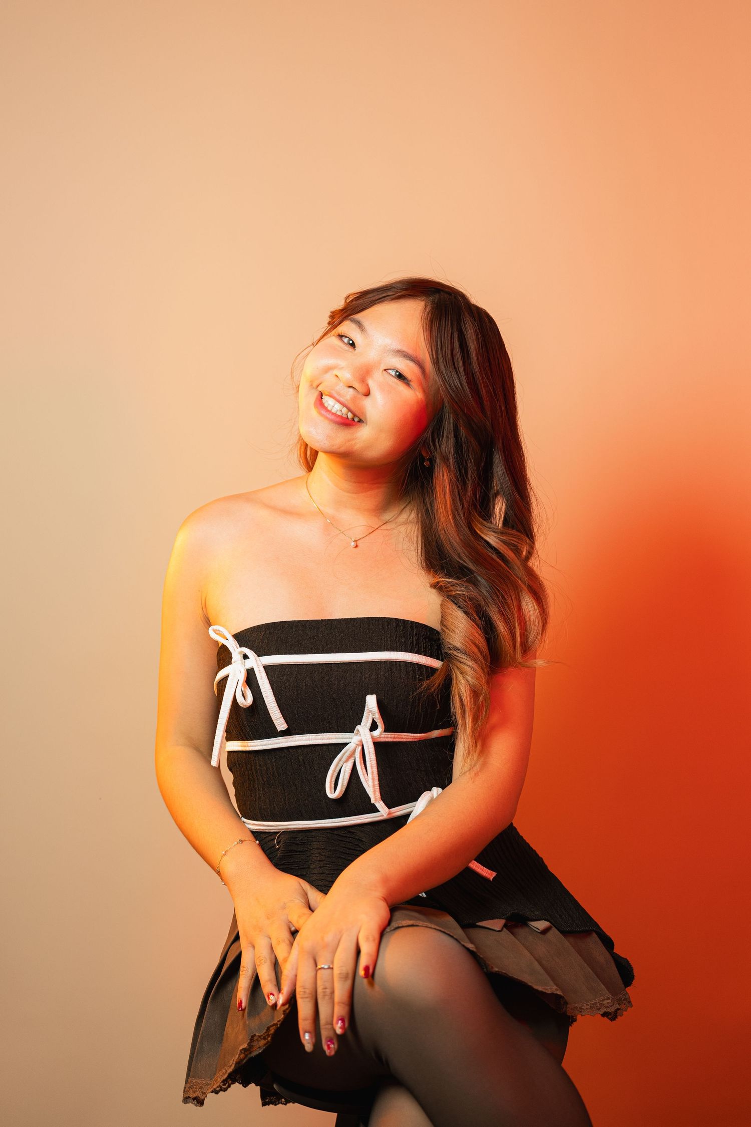 Fashion portrait against orange gradient backdrop featuring black strapless dress.