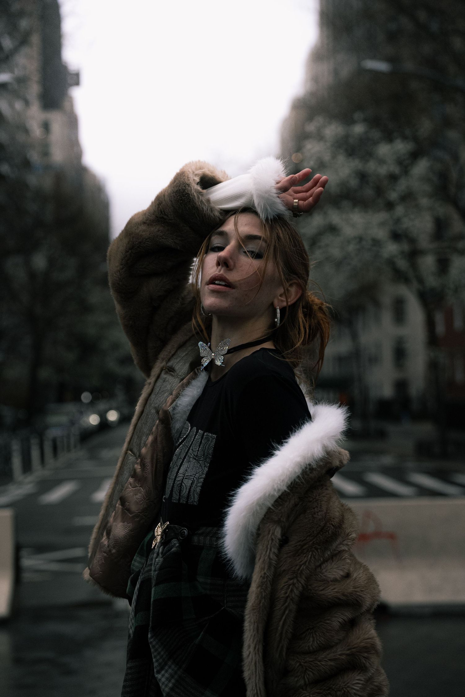 Dramatic portrait in urban setting with person wearing fur coat against moody city backdrop.