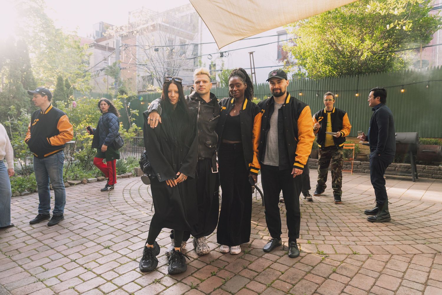 Group of people in dark clothing gathered outdoors on brick paved area.