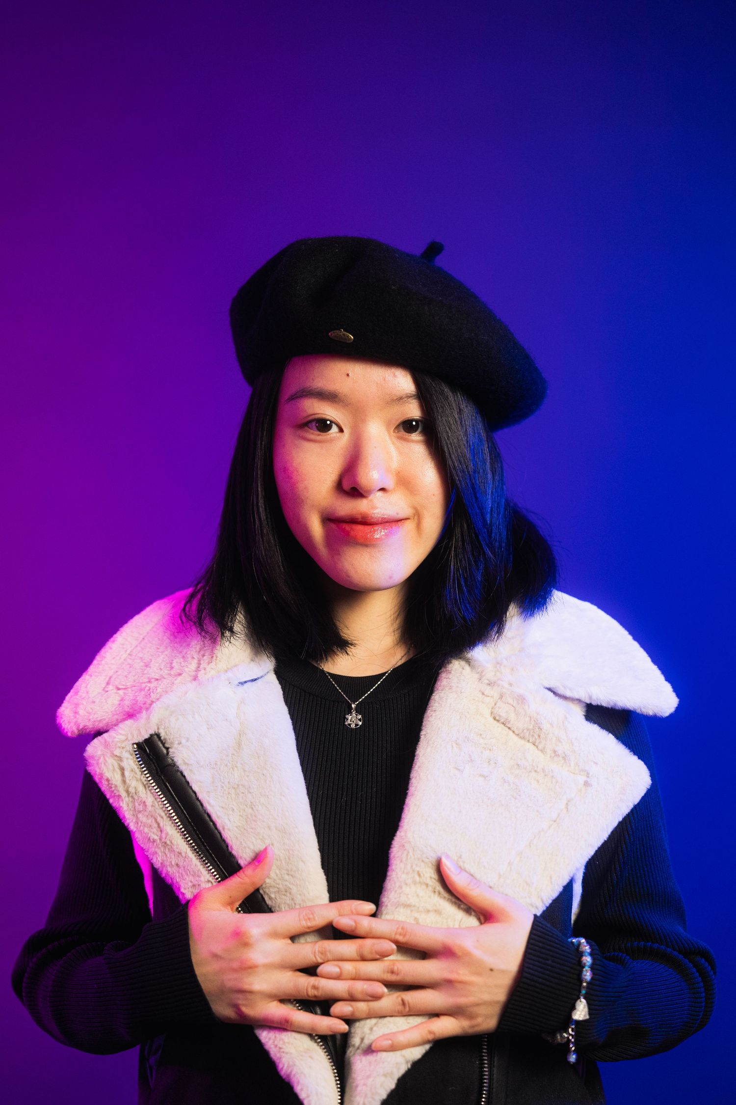 Portrait with purple and blue lighting wearing beret and white fuzzy jacket.