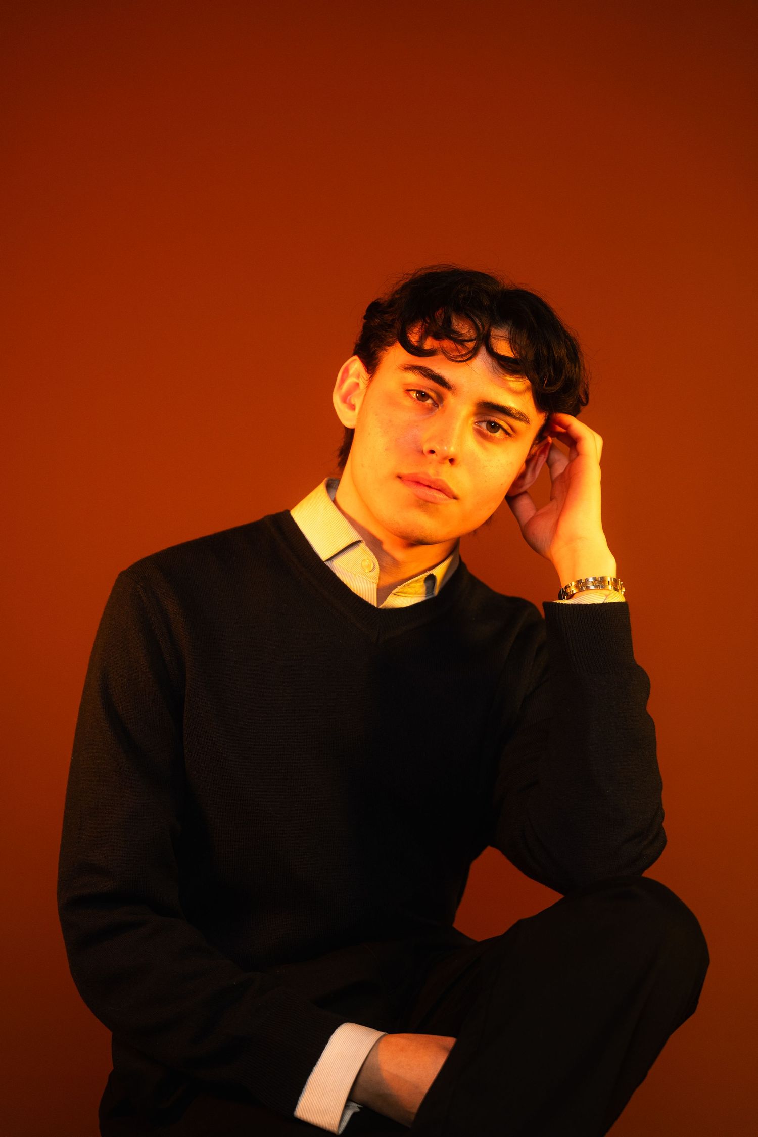 Dramatic portrait against warm orange backdrop in dark formal attire.