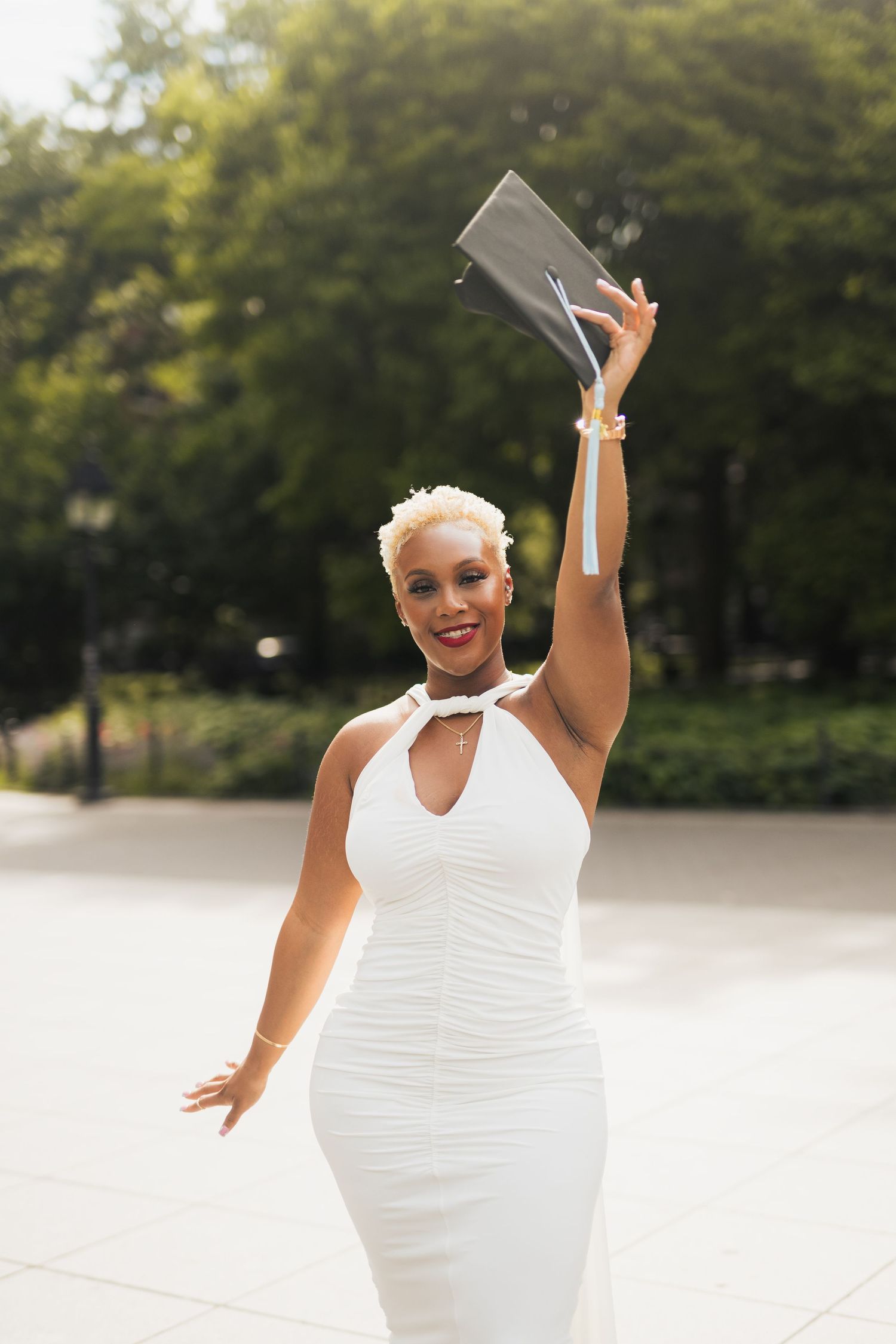 Joyful outdoor photoshoot featuring a person in white dress with raised arms against green foliage.