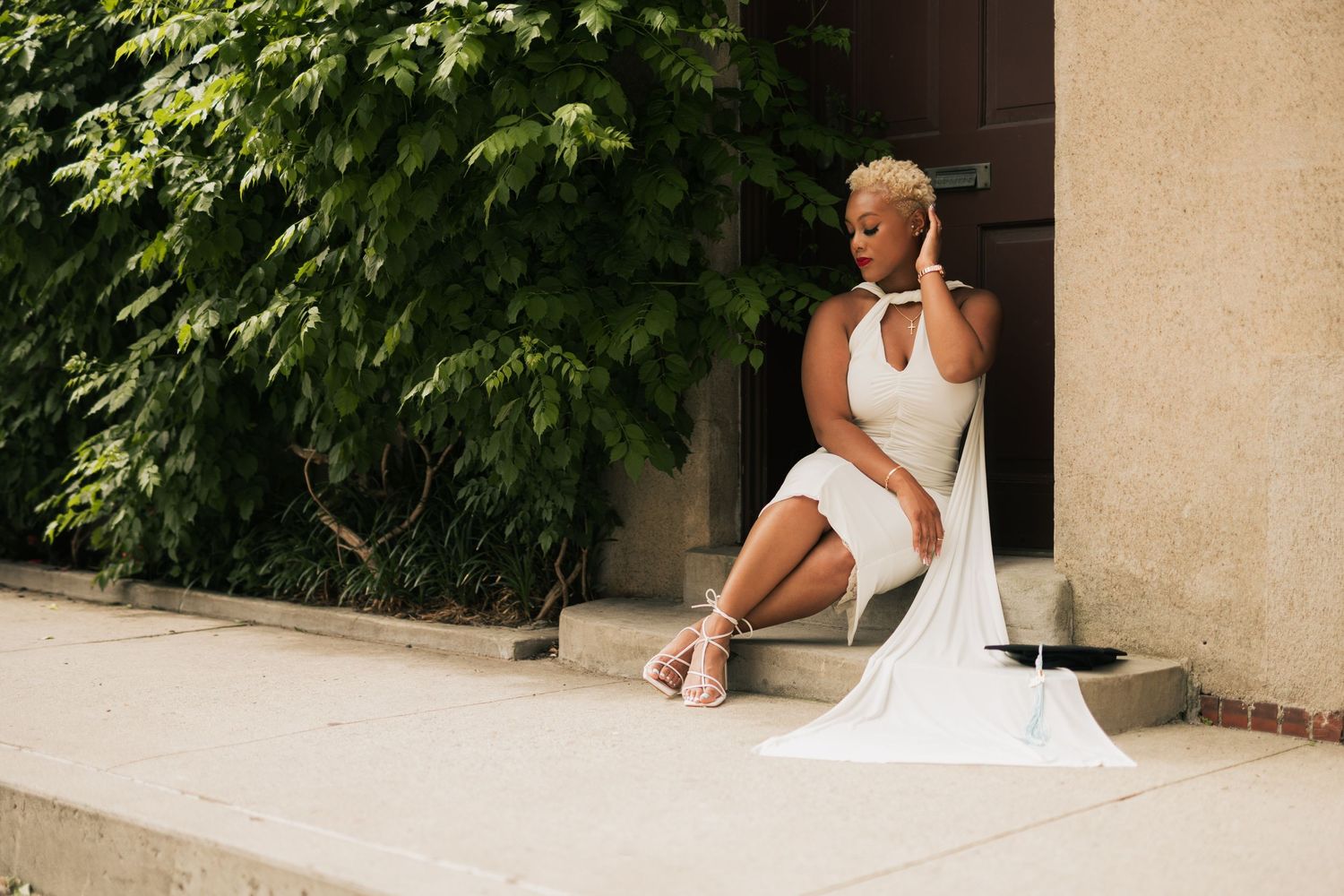 Outdoor portrait series with white dress against architectural elements and green trees.