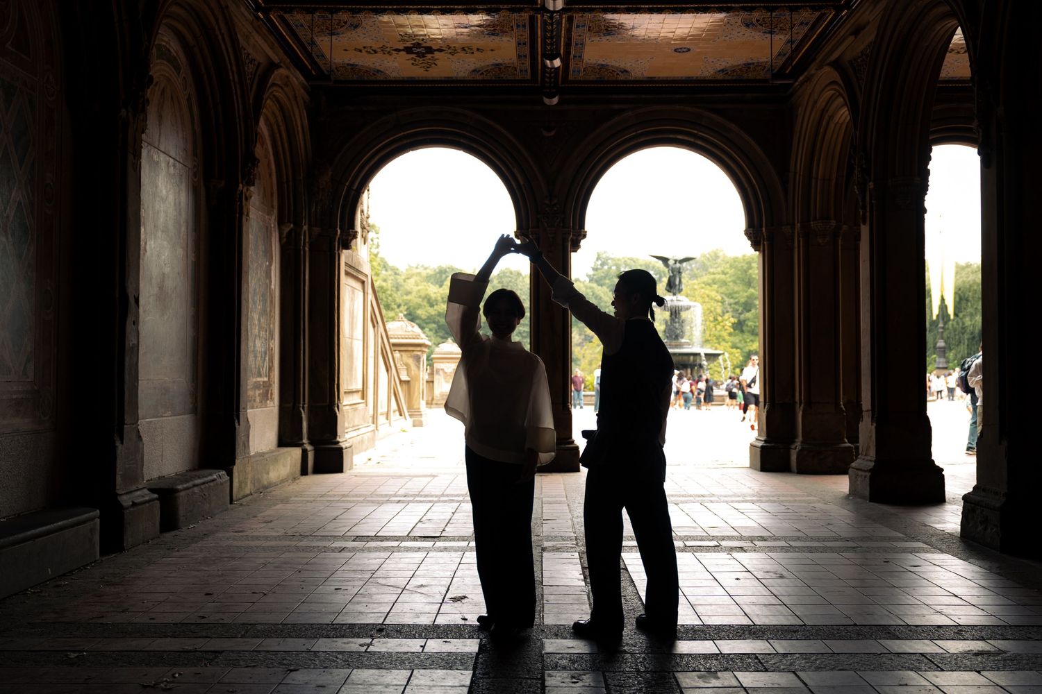 Silhouettes of people walking through a dimly lit colonnade or covered walkway.