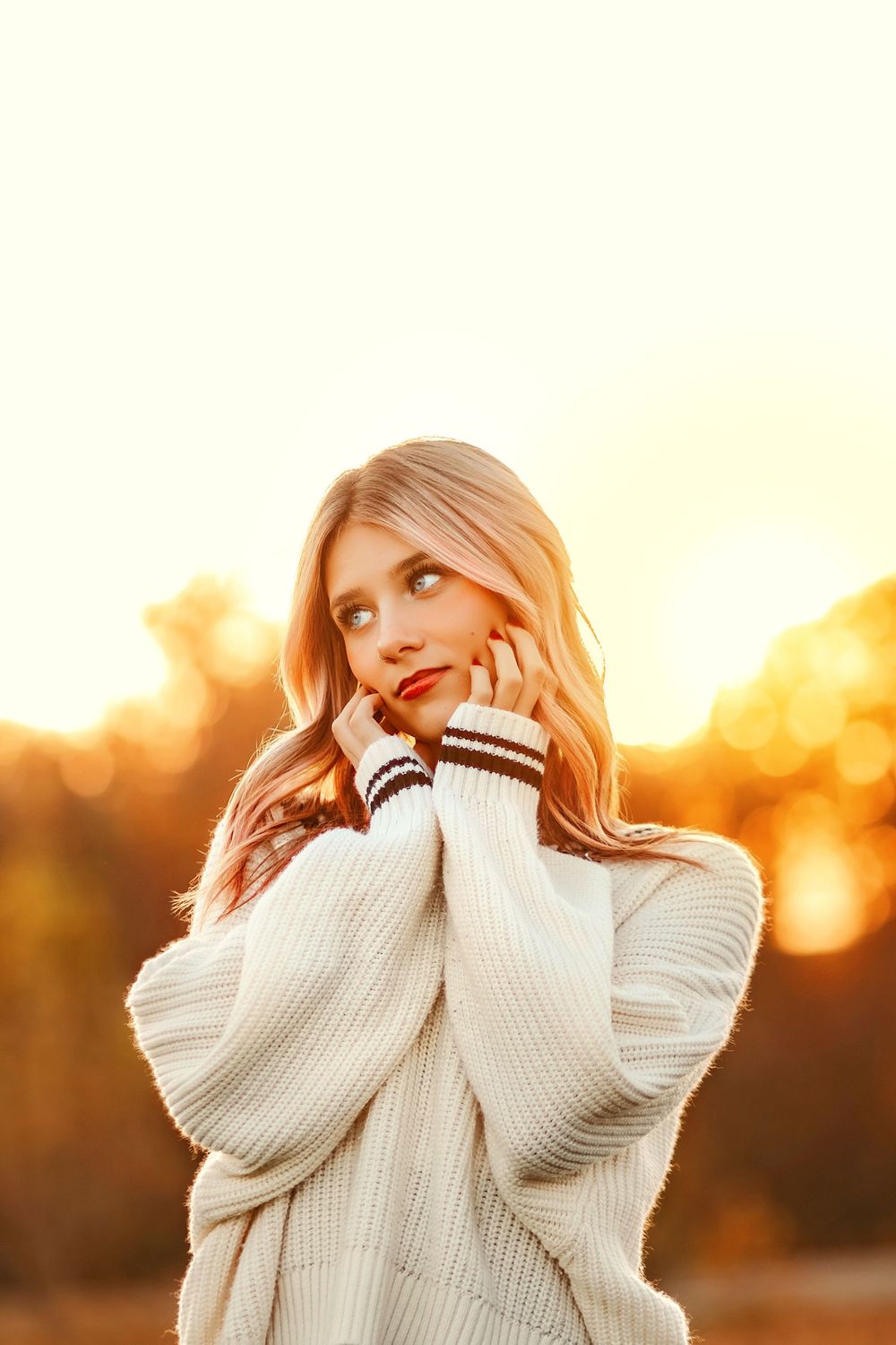 Blonde teenage girl in oversized cream knit sweater posing outdoors in warm golden sunset glow. Codorus Fall Senior Pictures