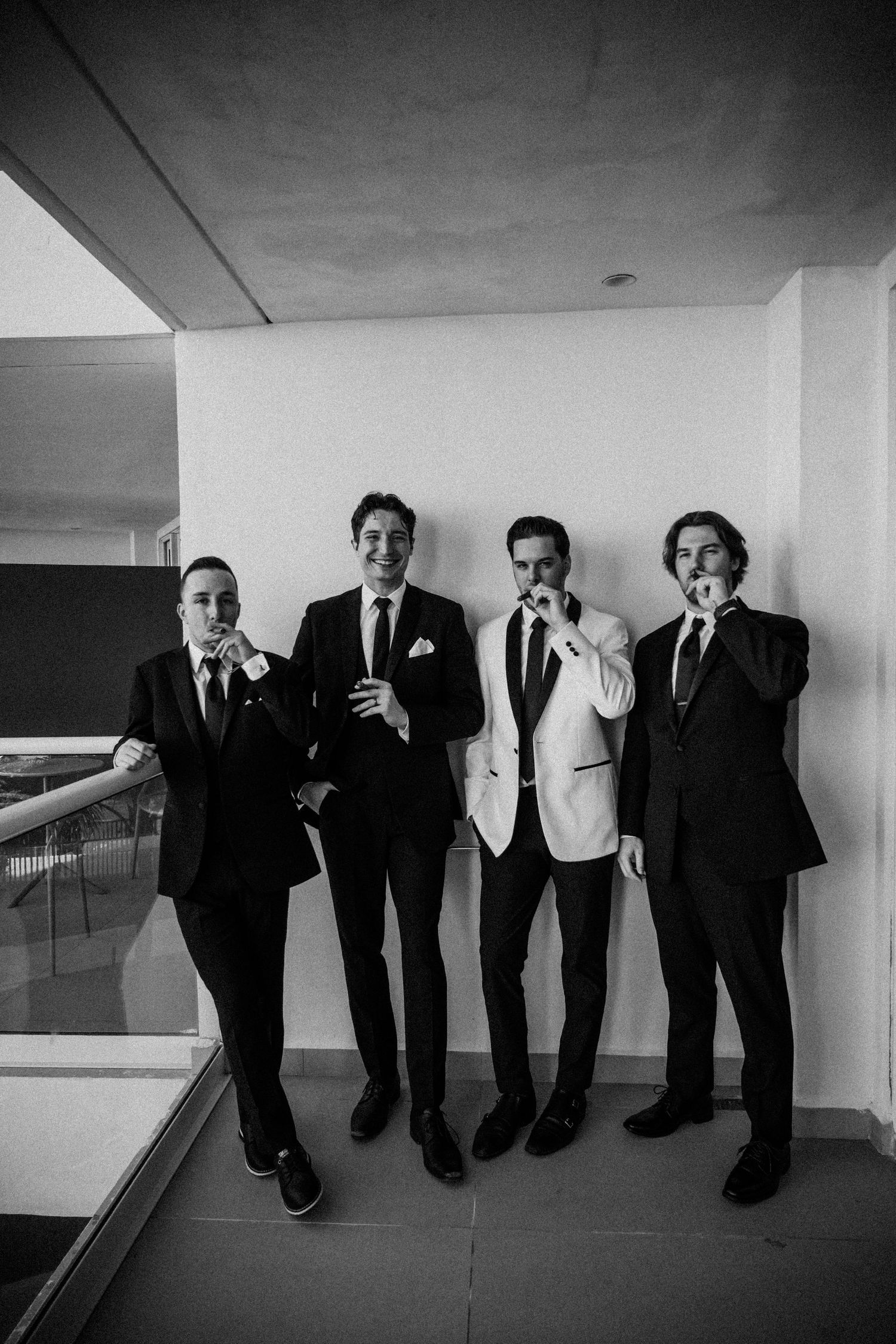 Four men in formal suits posing together in a hallway, black and white wedding photo.