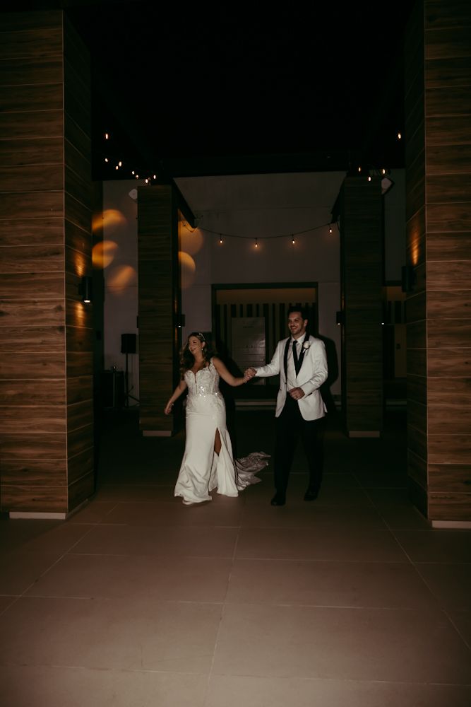 Bride and groom holding hands walking through elegant venue entrance with string lights at night.