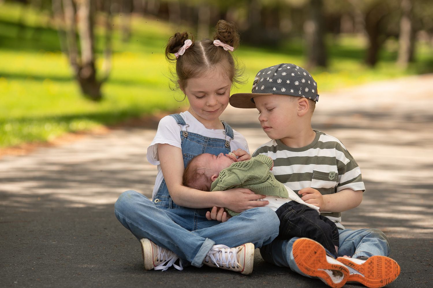 Children sitting on sidewalk looking at a book together on sunny day in park.