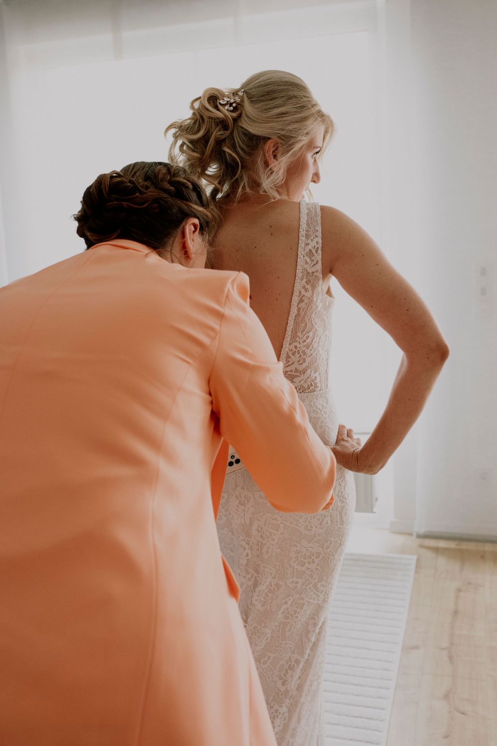 Getting ready scene showing final dress adjustments in warm natural light.