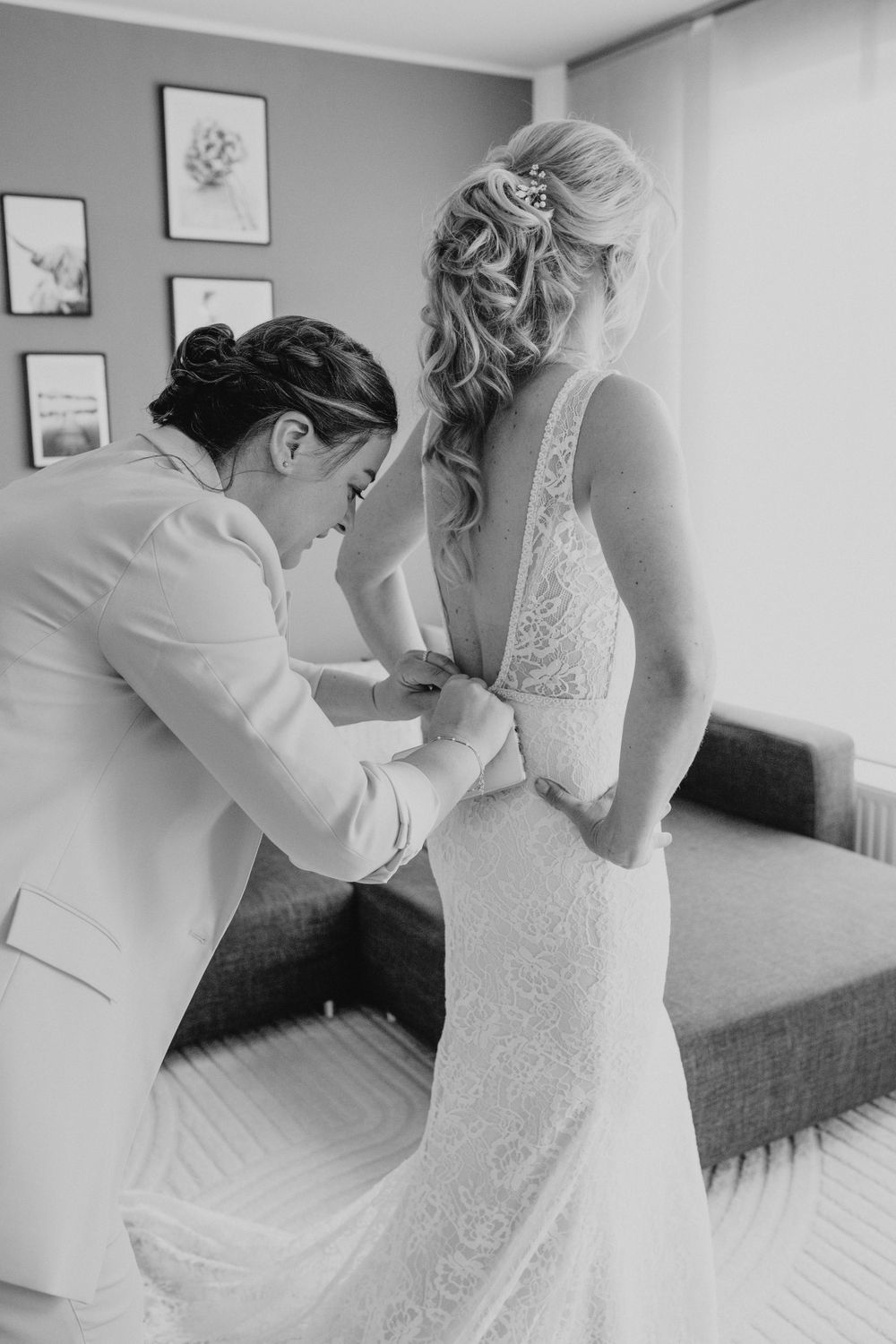 Black and white candid moment of wedding dress preparations in a bedroom.