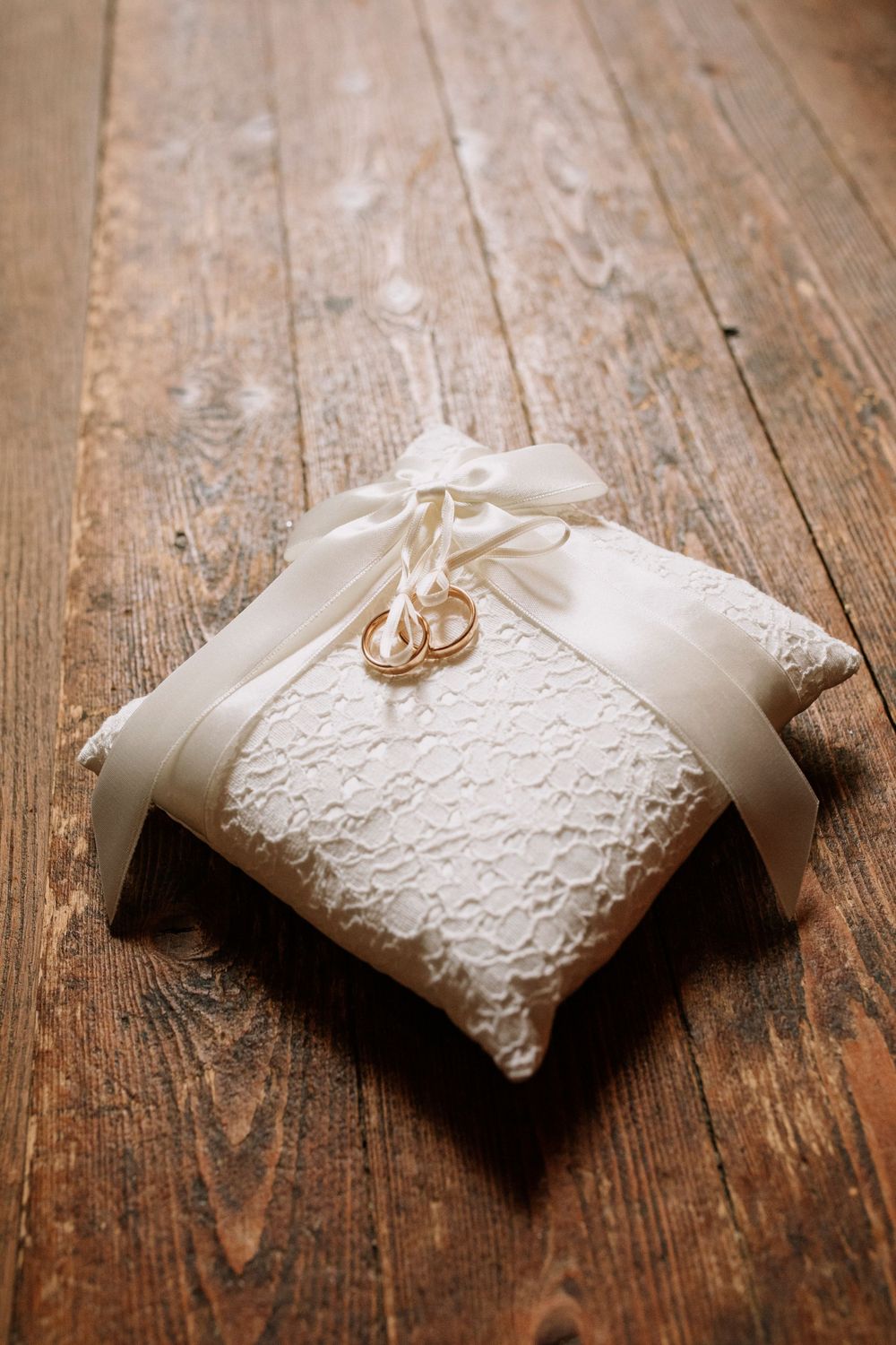 White lace ring bearer pillow with wedding rings displayed on rustic wooden surface.
