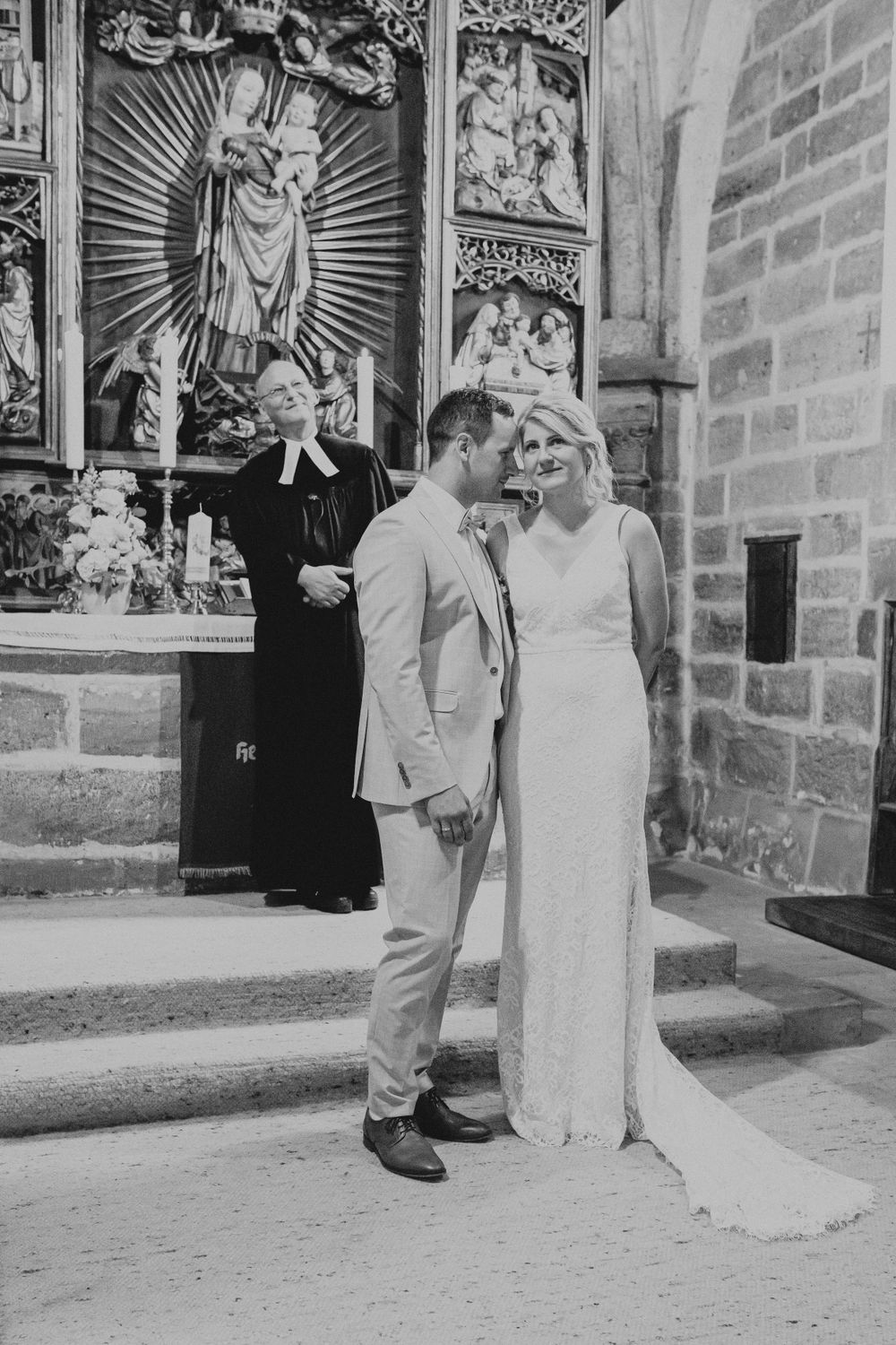 Wedding couple posing in front of ornate religious artwork and stone walls.