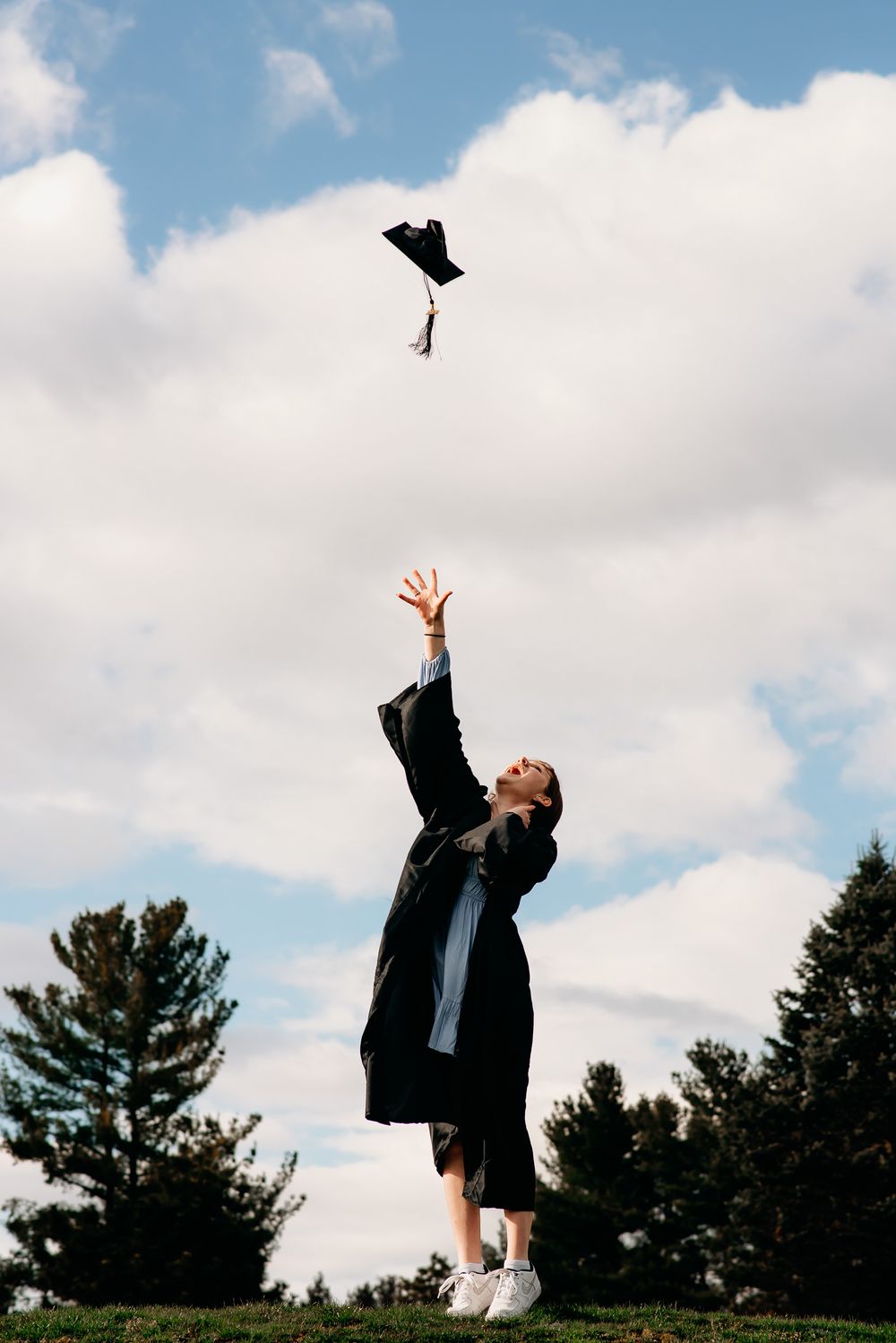 College graduate throwing cap in the air with a cloudy backdrop for portrait session