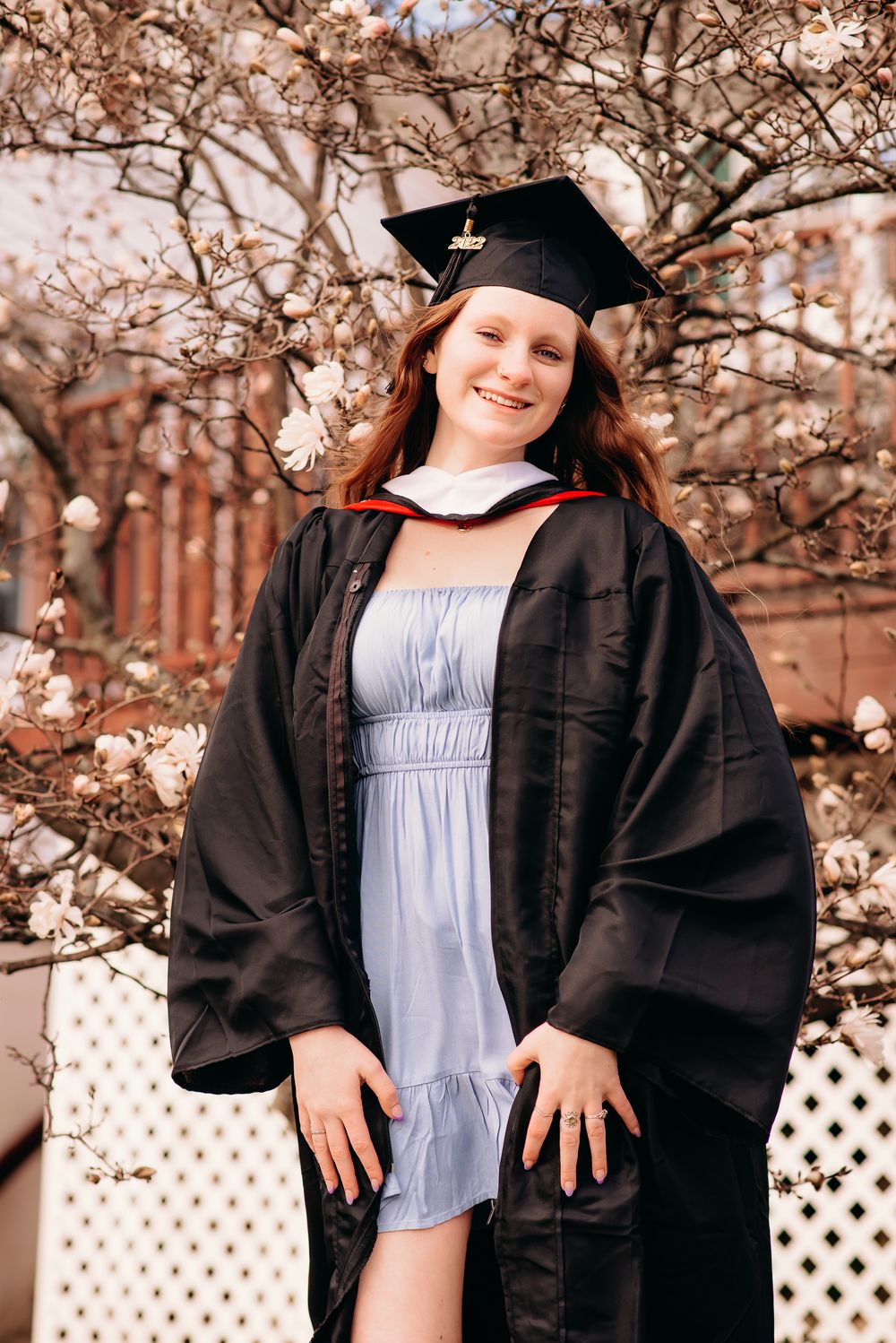 smiling college graduate dressed in cap and gown for outdoor portrait session