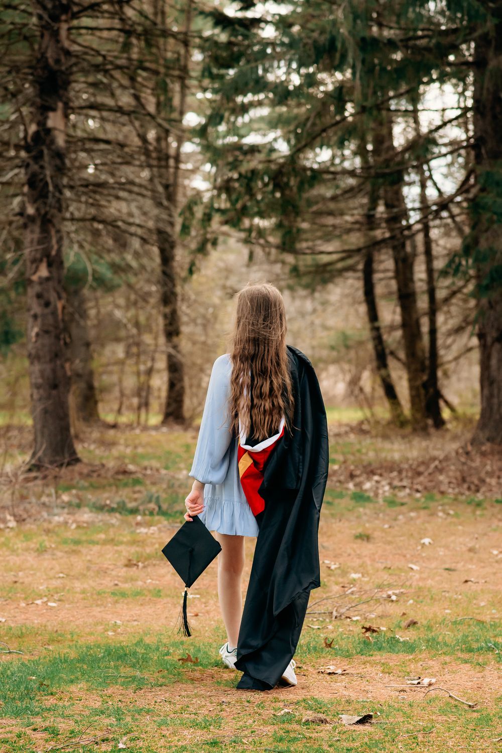 college graduate walking away from camera with cap and gown thrown over the shoulder