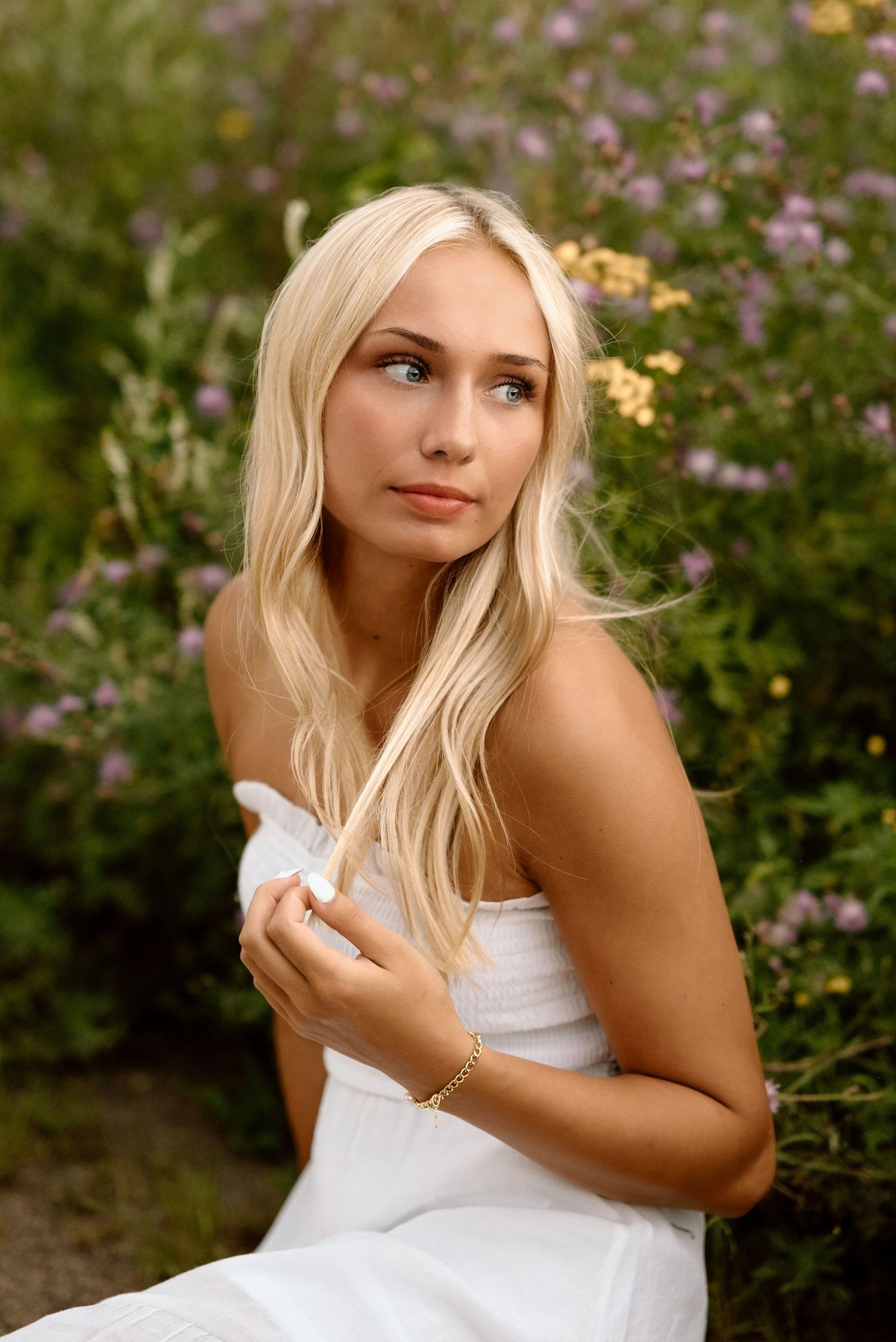 Portrait of person in white dress posing against blooming garden background during golden hour.